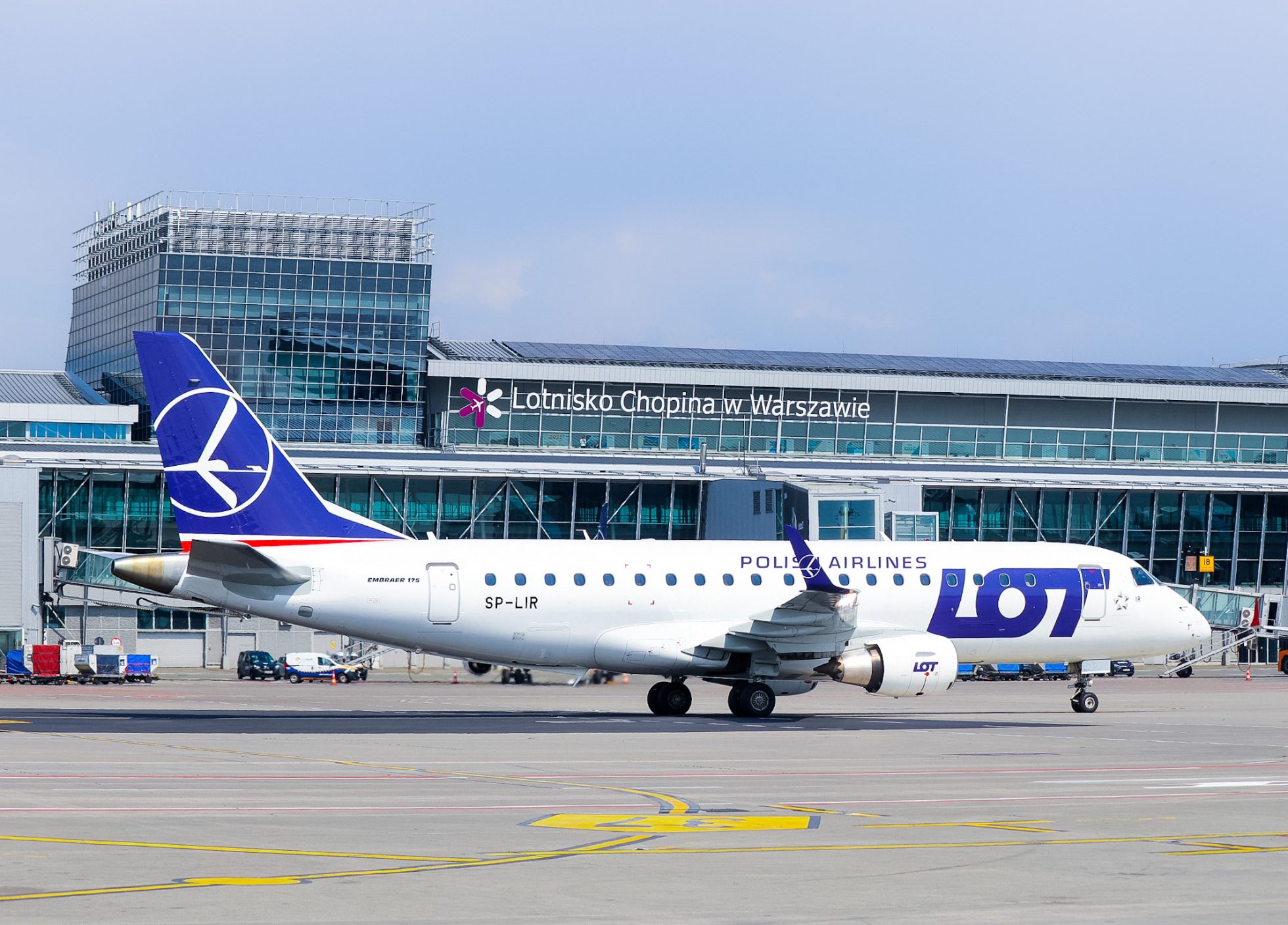 Embraer of LOT taxiing in front of Warsaw Chopin Airport terminal on a rainy day