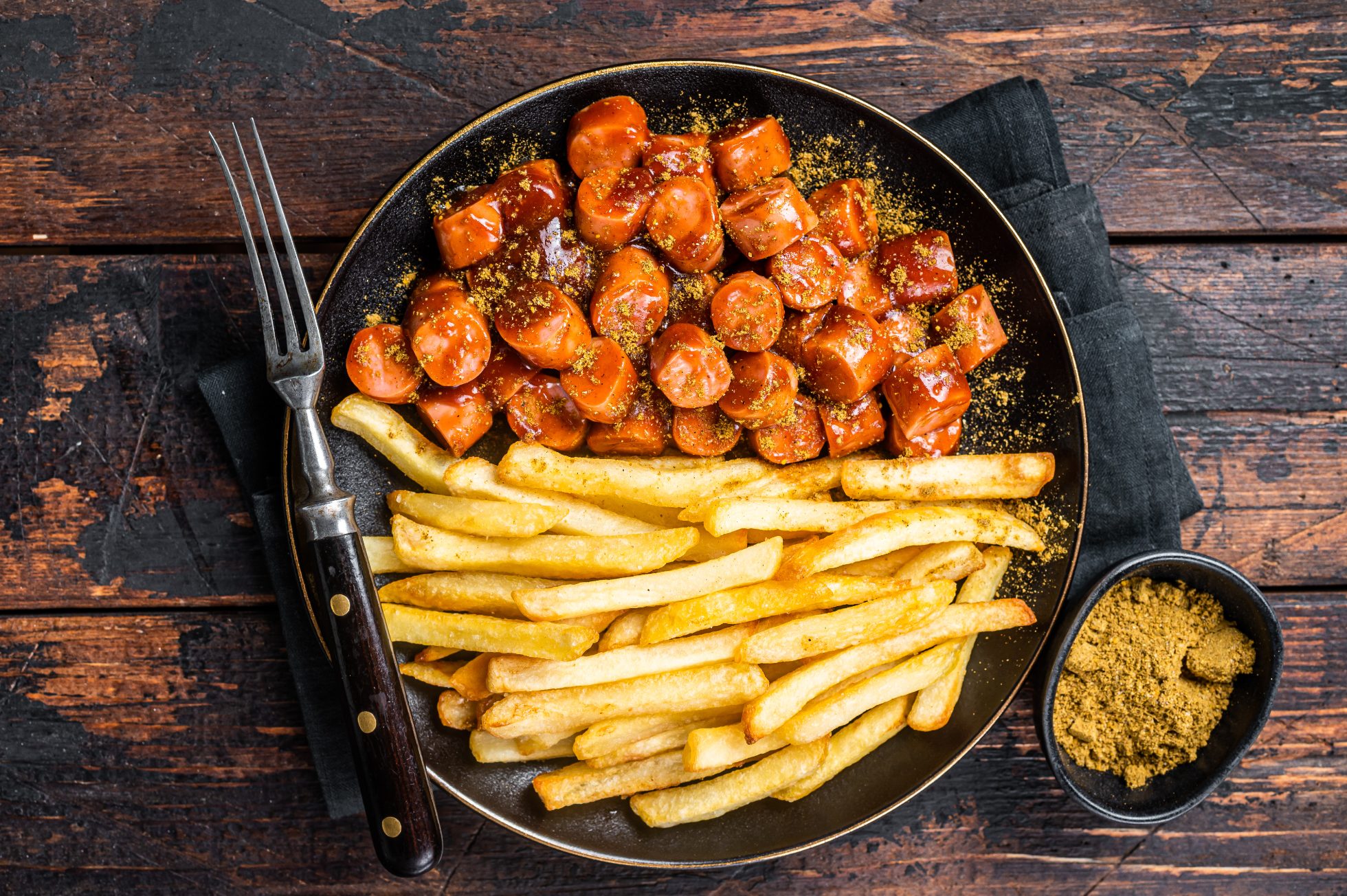 Klasyczne danie niemieckie - currywurst podane na białym talerzu z frytkami i sosem.