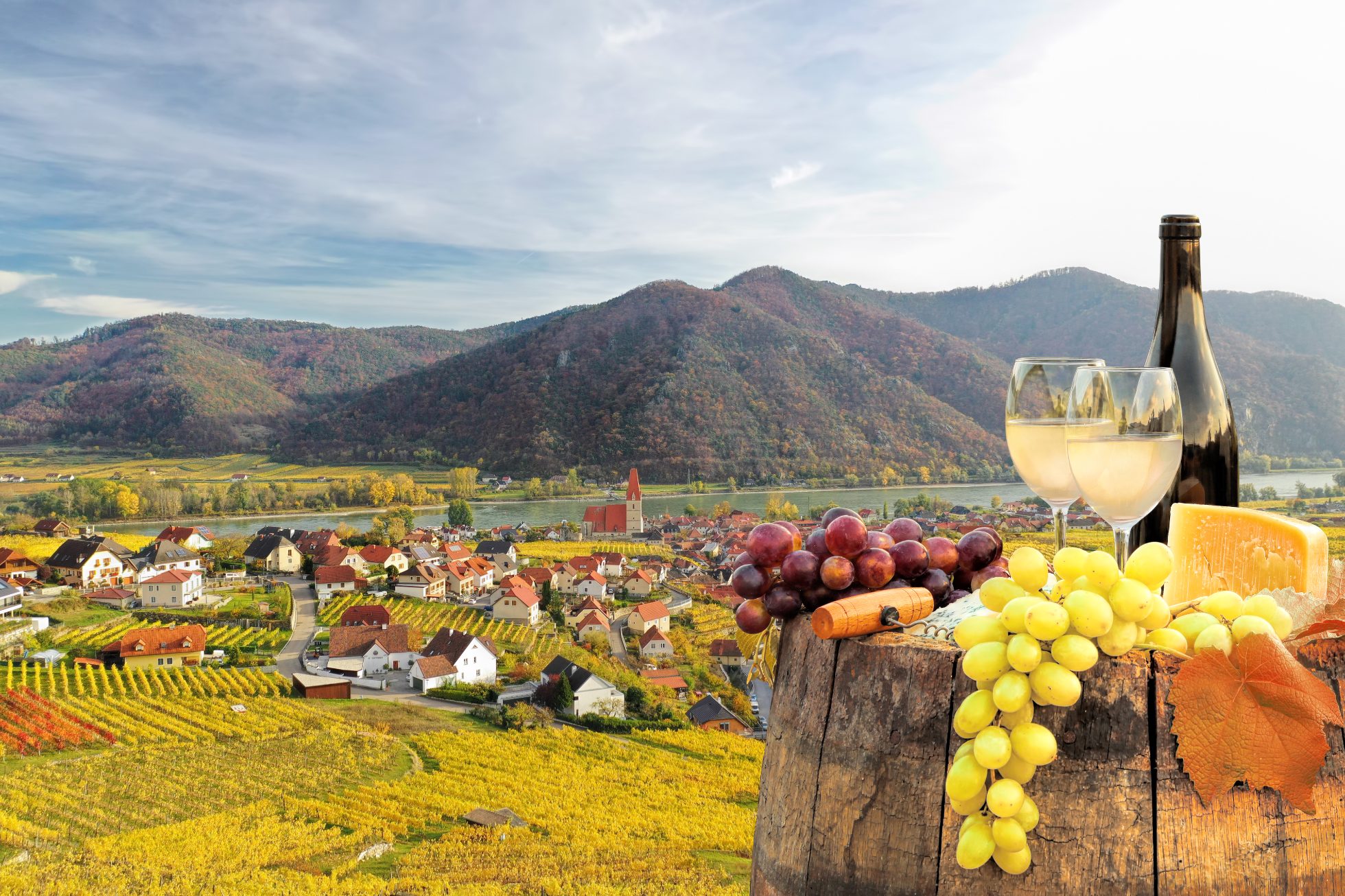 Butelka białego wina z kieliszkami na tle wioski Weissenkirchen z jesiennymi winnicami w dolinie Wachau, Austria.