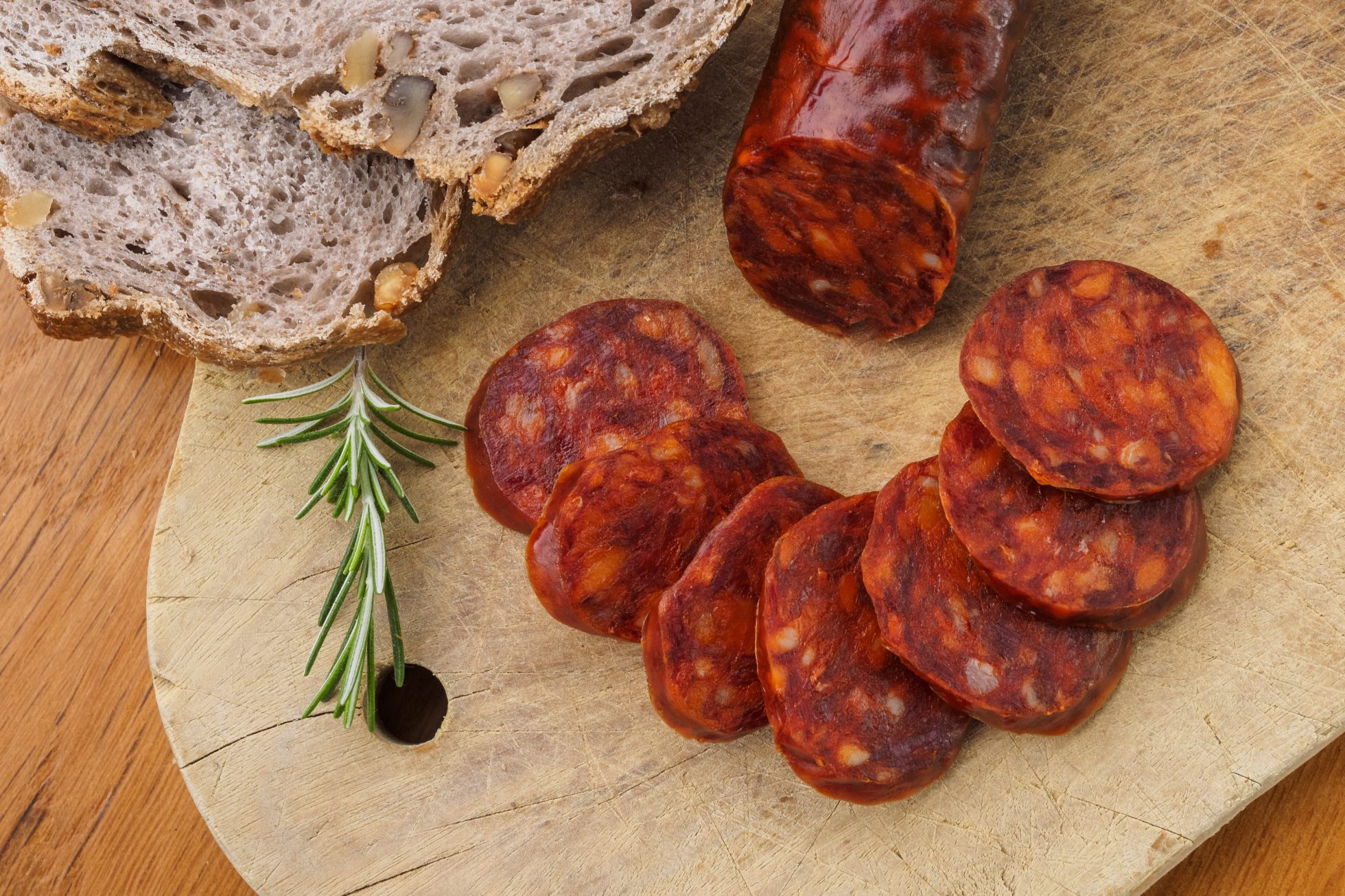 Chorizo iberyjskie, chorizo hiszpańskie lub hiszpańska kiełbasa pokrojona w plasterki na drewnianej desce, podana z rustykalnym chlebem