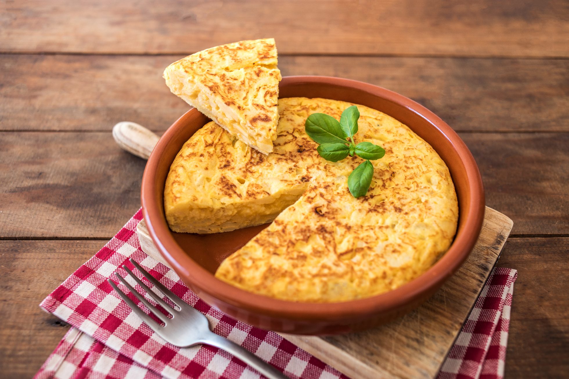 Hiszpański omlet ziemniaczany, zwany „tortilla de patatas”, na rustykalnym tle o fakturze drewna z miejscem na tekst