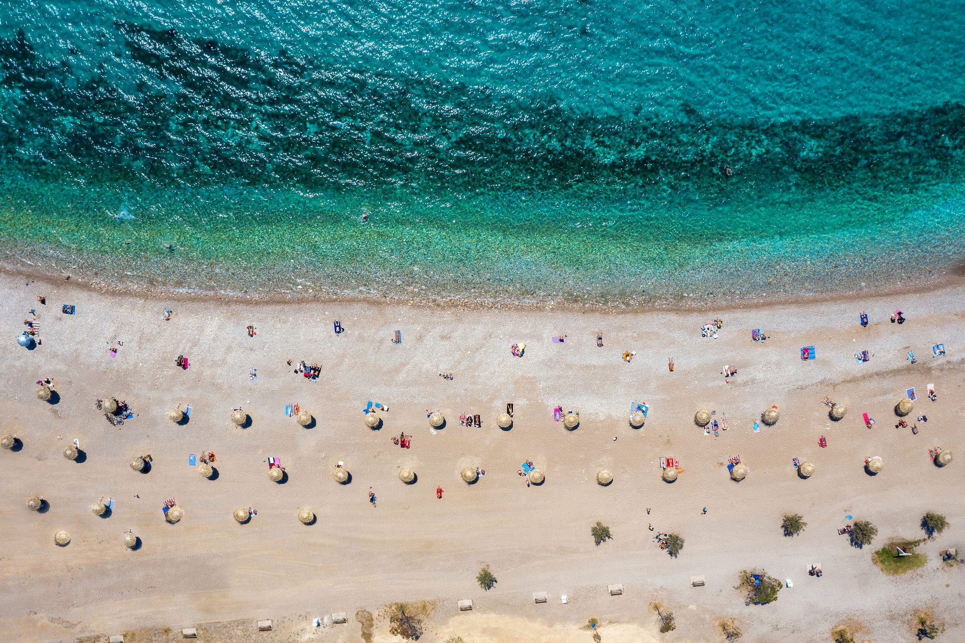 Widok z lotu ptaka z góry na plażę w dzielnicy Glyfada, na południu Riwiery Ateńskiej, w Grecji, z parasolami ustawionymi od siebie w ramach środków dystansowania społecznego Corona, ateny plaże