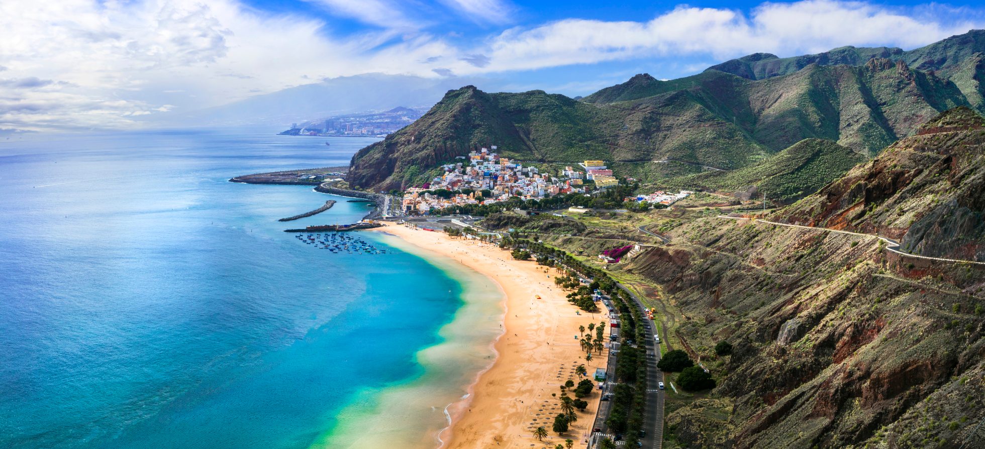 Wunderschöner Strand mit blauem Meer, goldenem Sand und Palmen. Berge im Hintergrund, klarer Himmel.