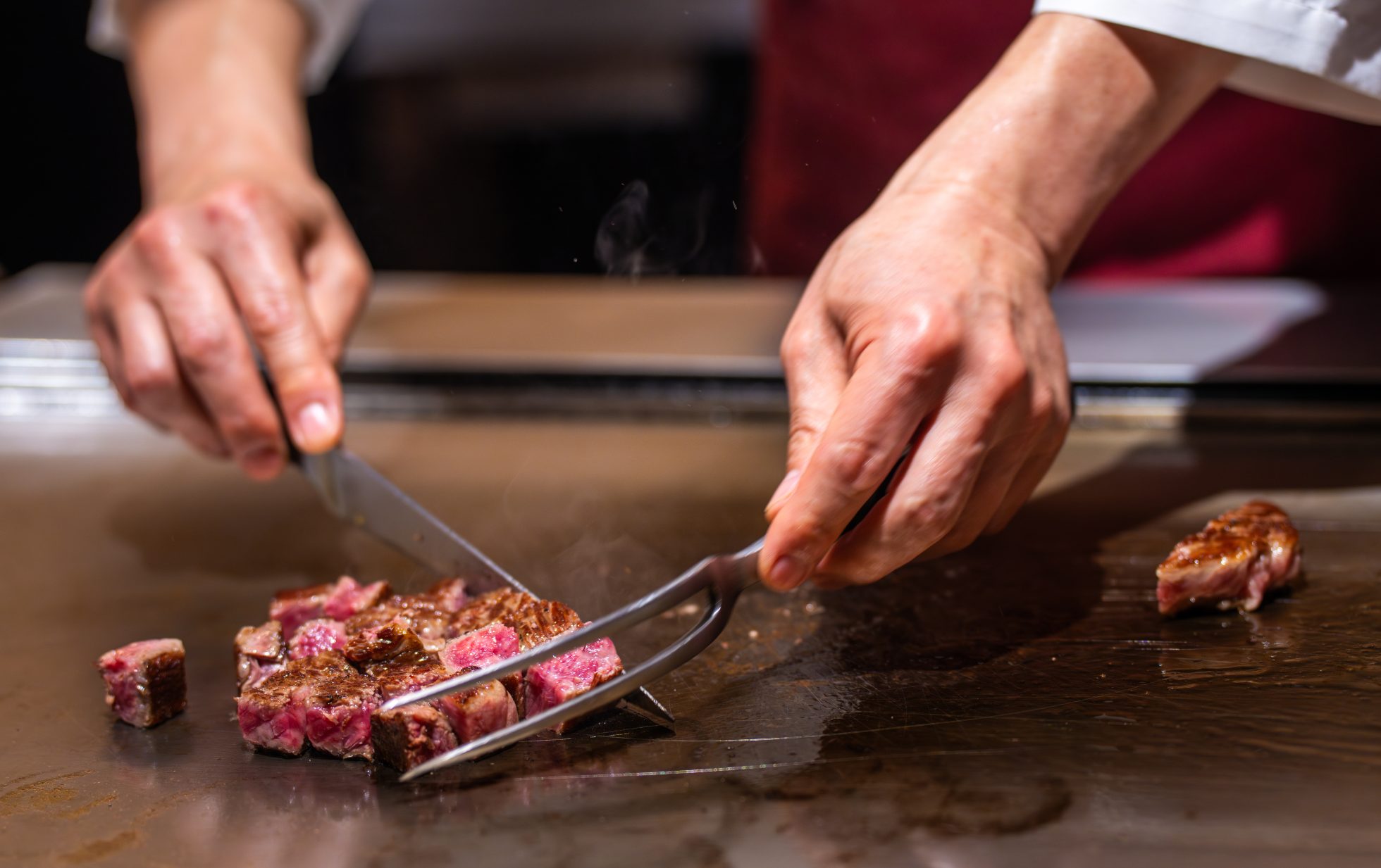 Zbliżenie na kucharza krojącego stek z wołowiny wagyu o stopniu wysmażenia „medium-rare” na rozgrzanym żelaznym ruszcie za pomocą ostrego noża i widelca