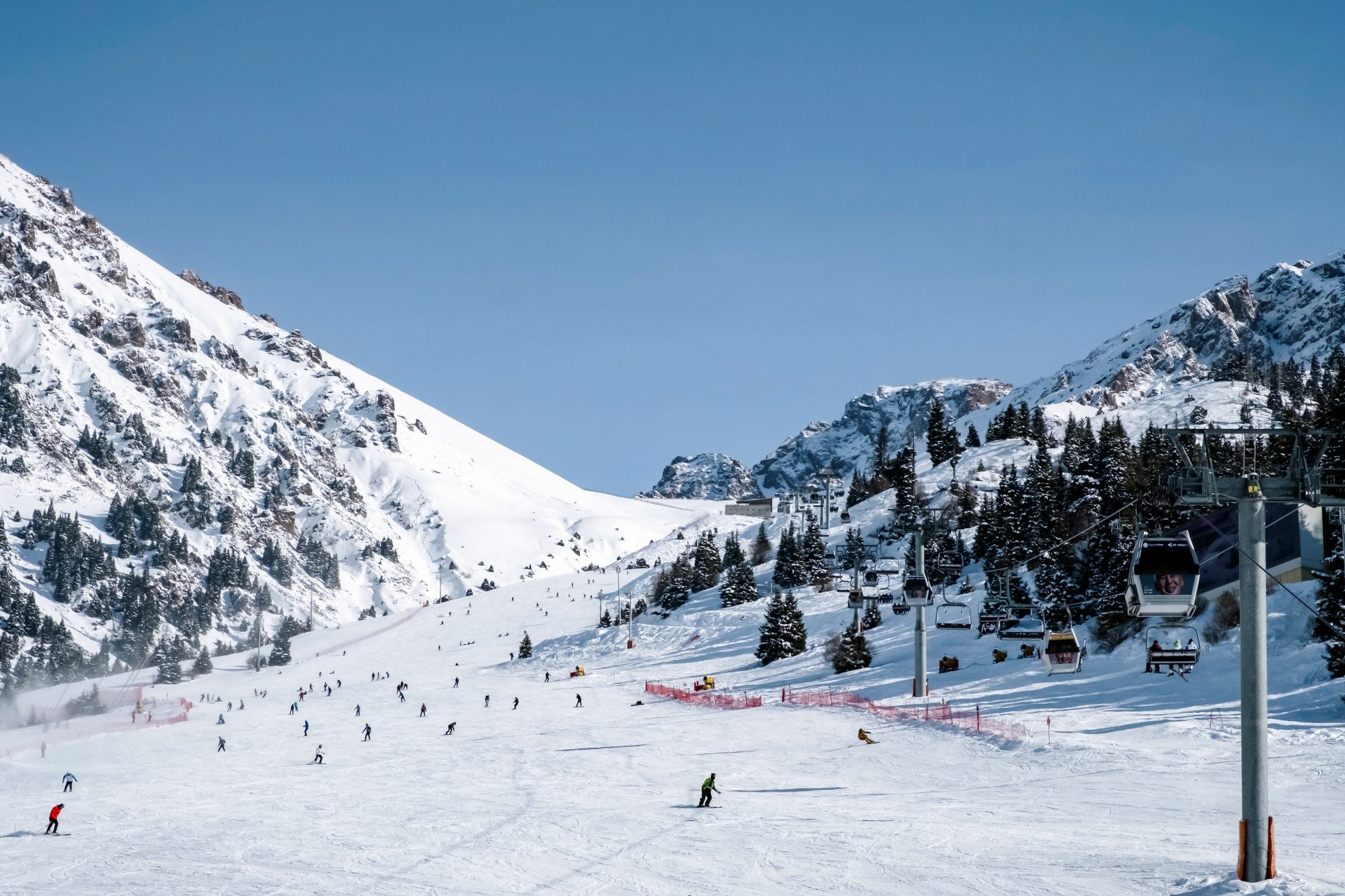 Shymbulak mountain resort's ski slopee with skiers and snowboarders.