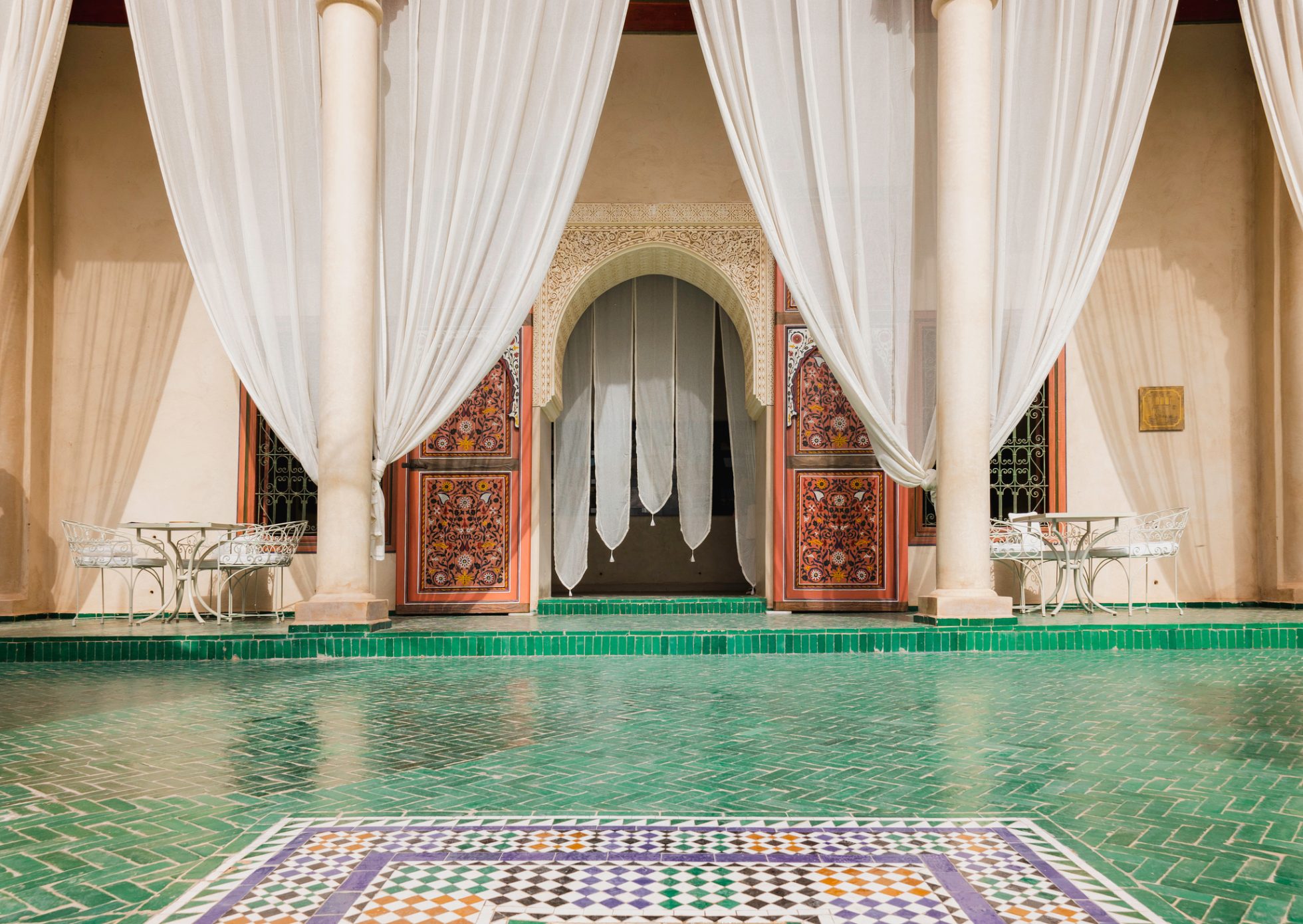 elegancki dziedziniec w Le Jardin Secret w Marrakeszu z zielonymi mozaikami, białymi zasłonami i misternym marokańskim wzornictwem, tradycyjną architekturą i spokojnym wystrojem na zewnątrz