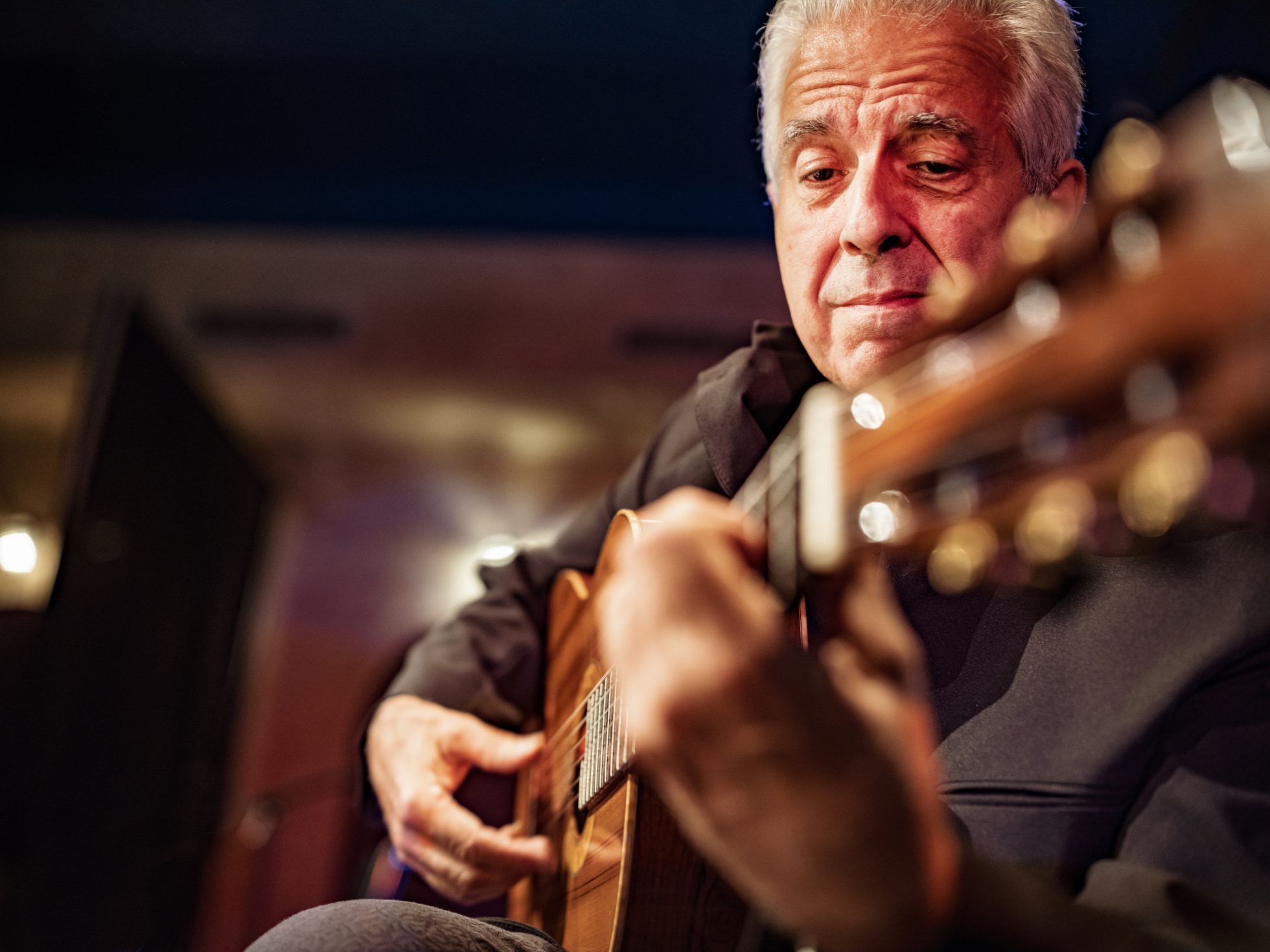 Osoba grająca na gitarze w tradycyjnym stroju, na tle kolorowych świateł, w czasie koncertu fado.