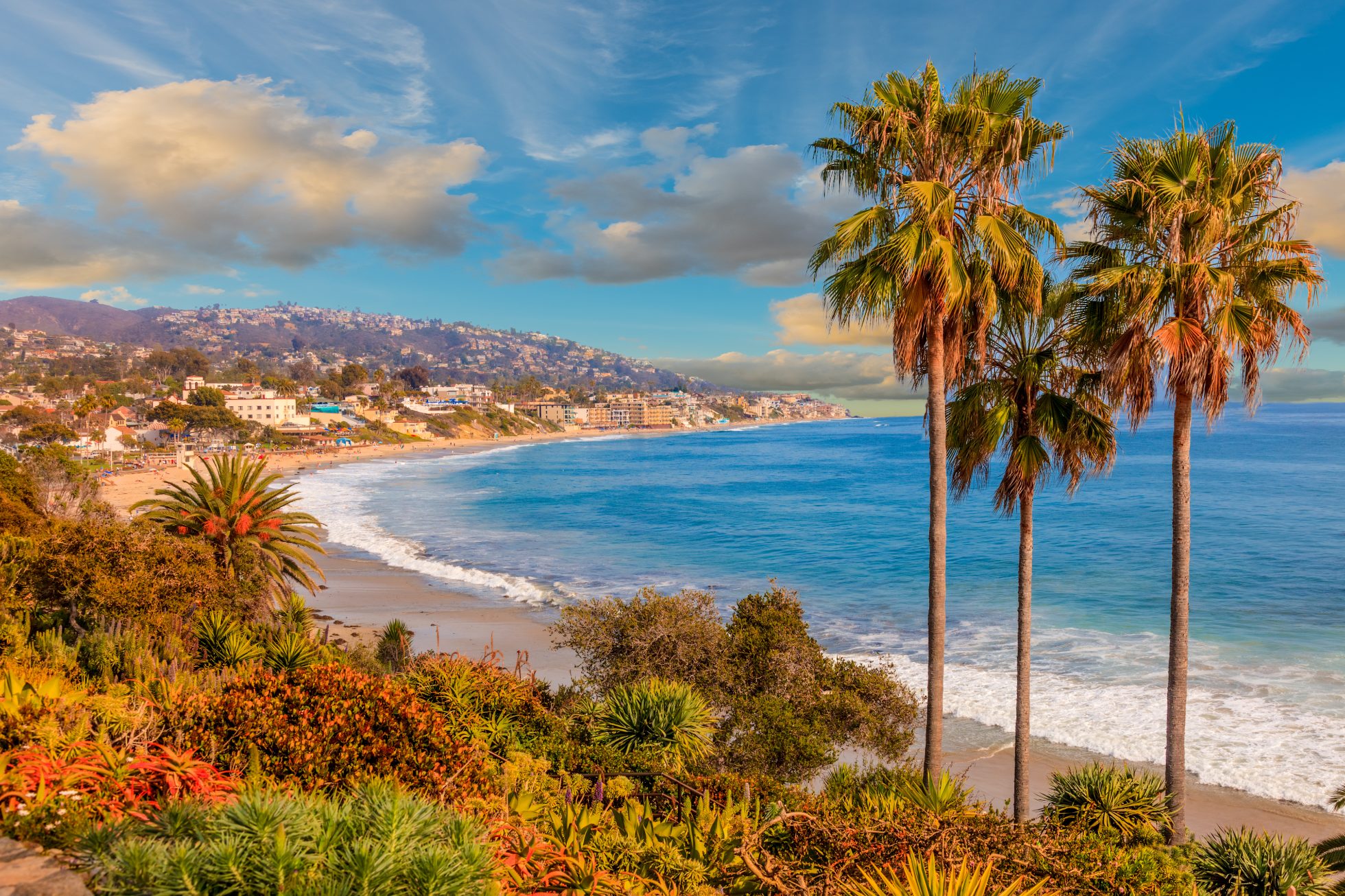 Plaża w Laguna Beach, Kalifornia. Błękitne morze, złoty piasek i skaliste wybrzeże. Słońce na niebie, palmy i parasole plażowe.