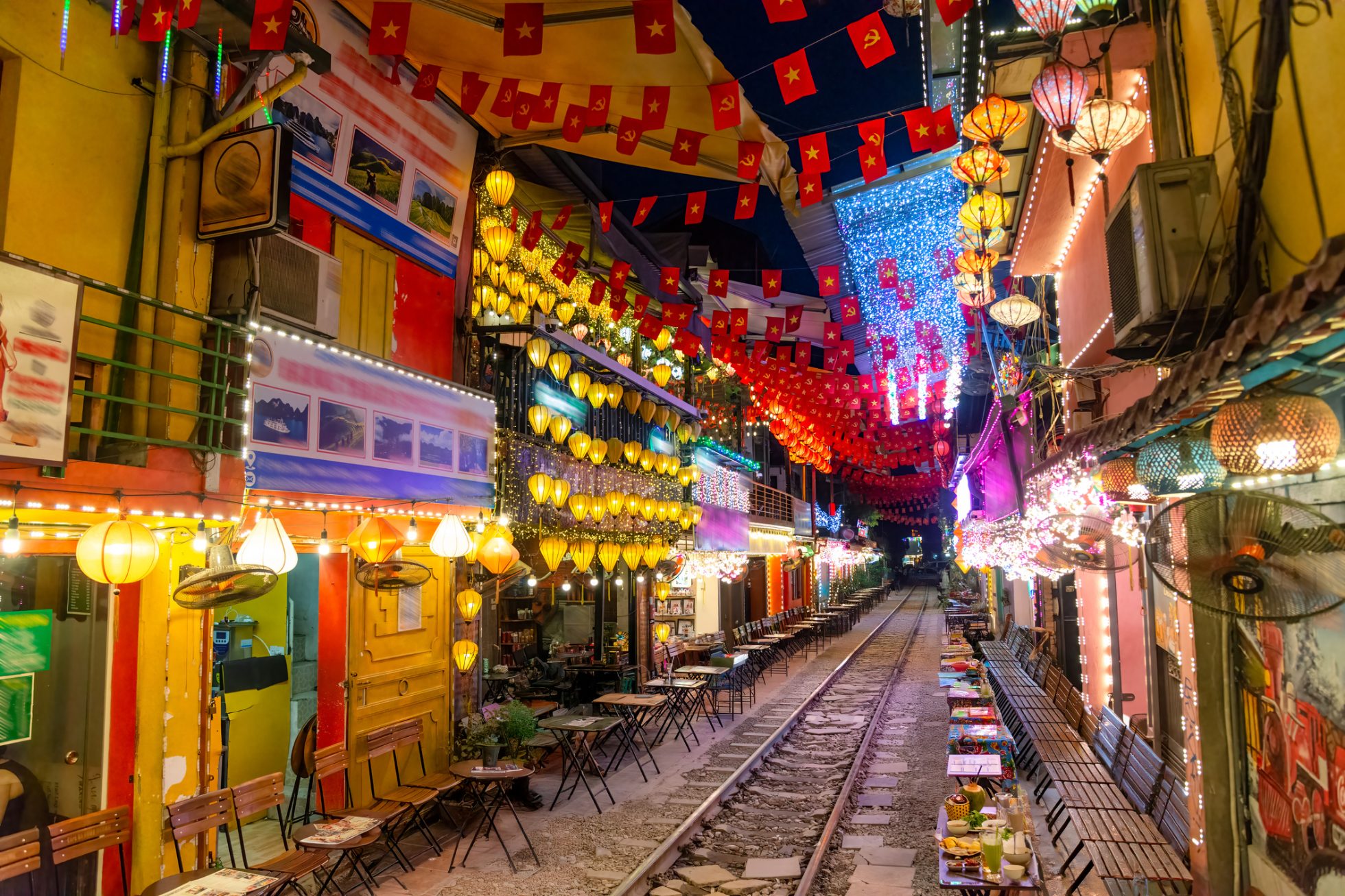 Tourists and locals enjoy coffee and drinks along Hanoi's famous Train Street, glowing with colorful lights and festive decor.