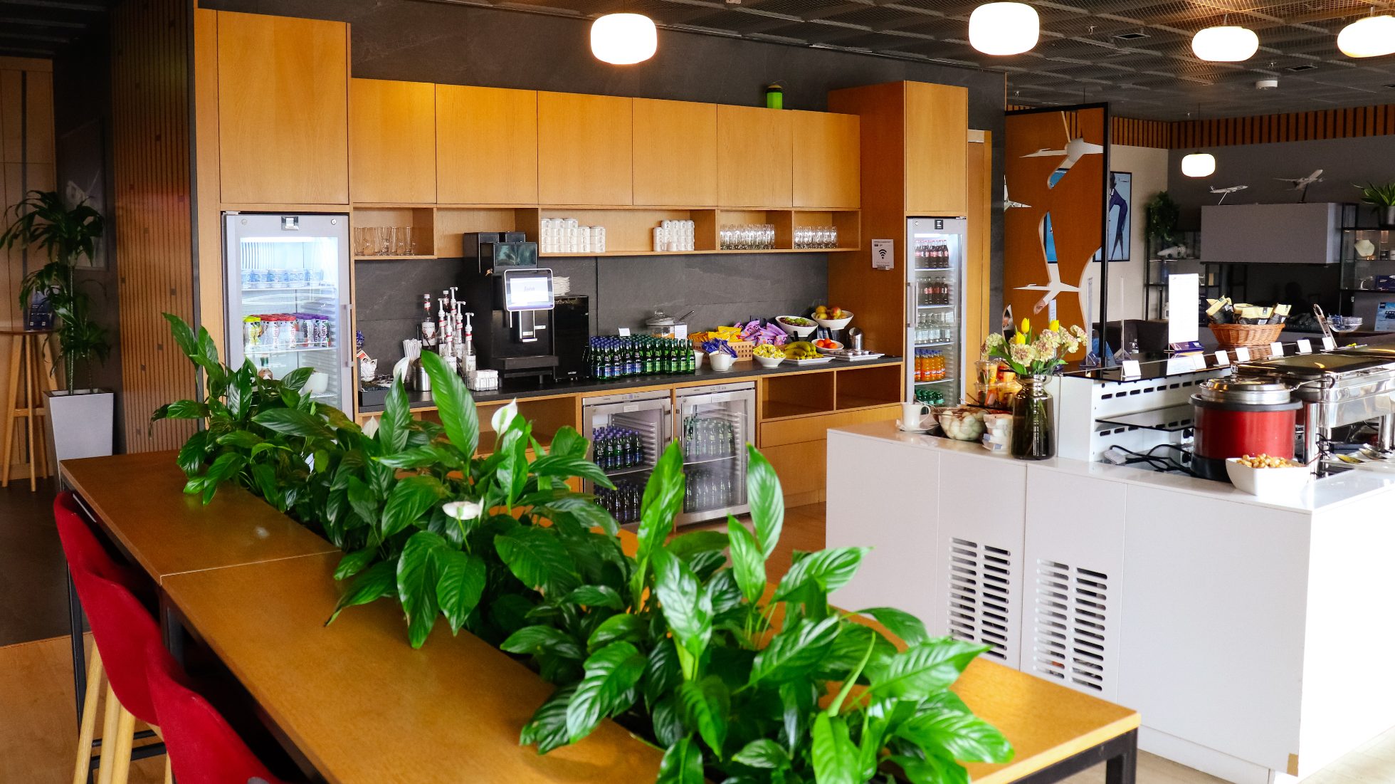 LOT Business Lounge Mazurek - hoher, länglicher Tisch mit Stühlen, Bar und Insel mit Snacks und Bemars