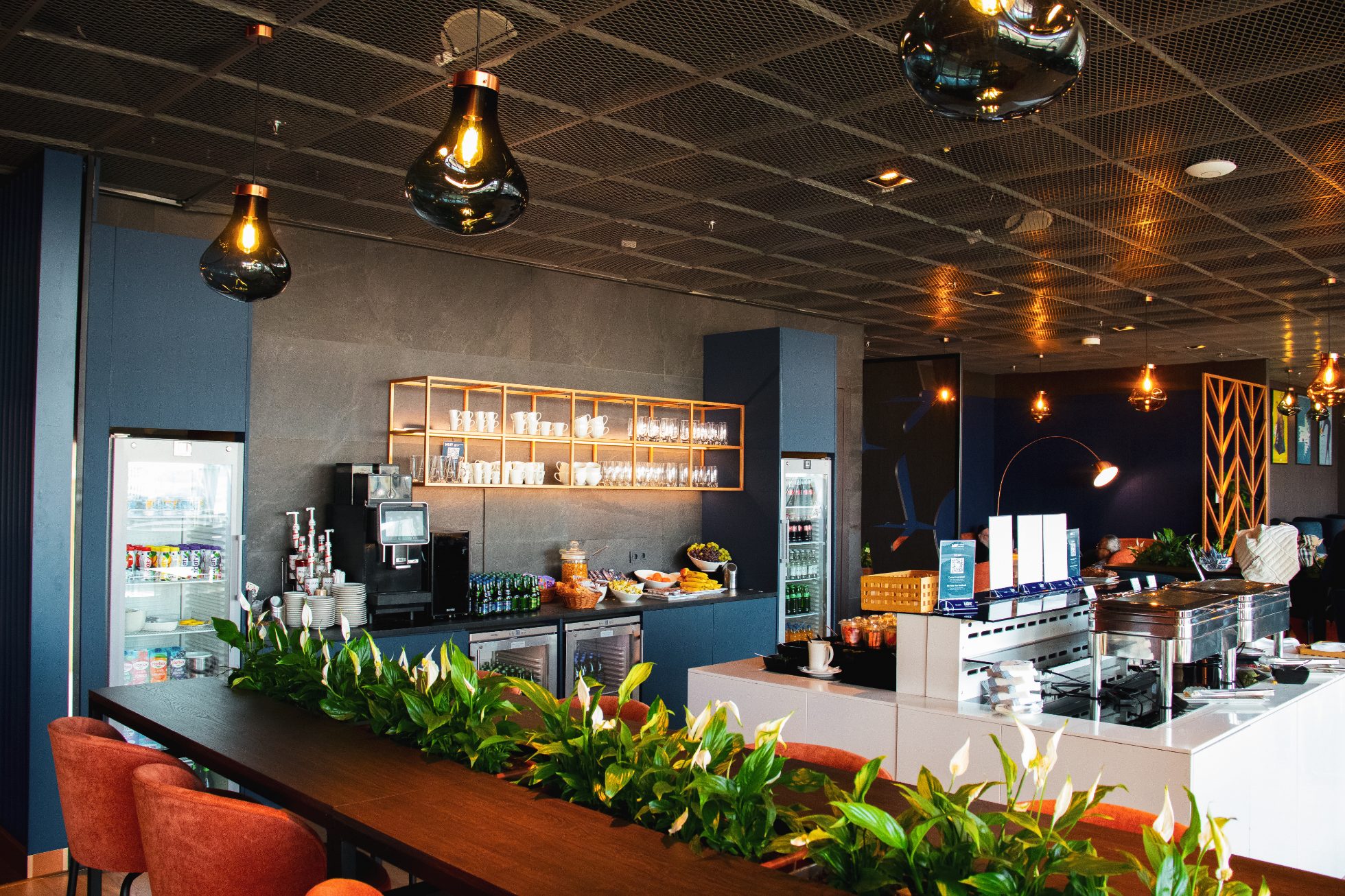 The interior of the Mazurek Business Lounge – an island with a dining area and a bar serving drinks and snacks