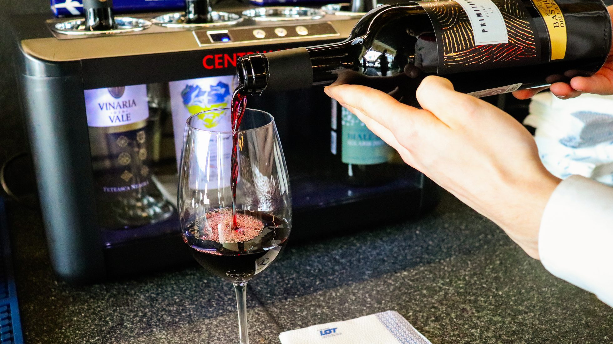 A man's hand holding a bottle of red wine and pouring into a glass