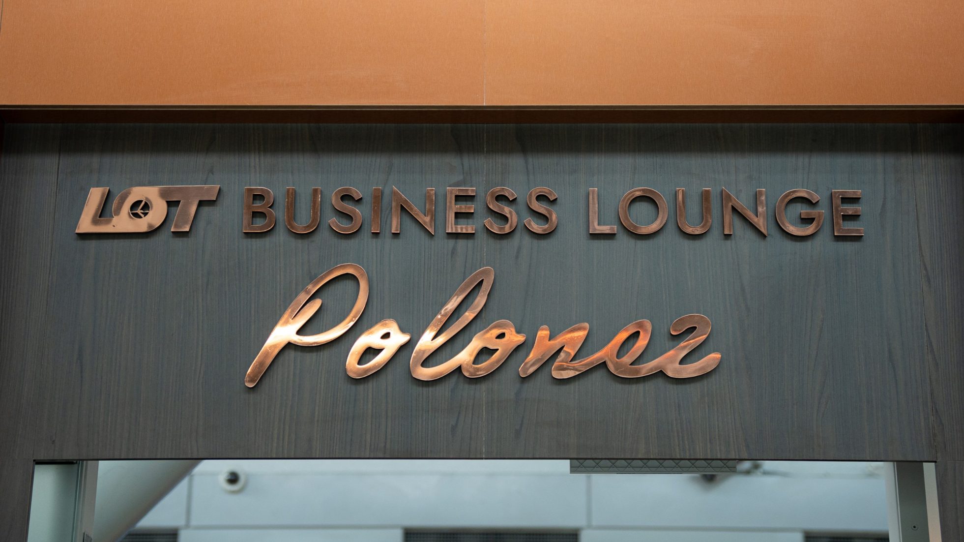Złote logo LOT Business Lounge Polonez na szarym tle na lotnisku w Warszawie