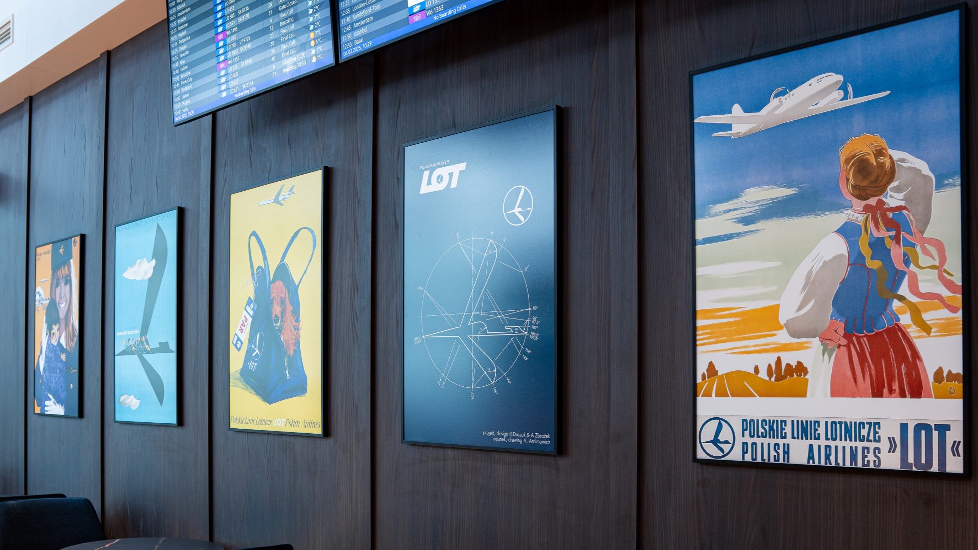LOT Business Lounge Polonez - Recepcja, otwarta przestrzeń ze stolikami i fotelami w kolorze granatowym, granatowe ściany z plakatami LOT-u. Strefa gastronomiczna oraz bar 