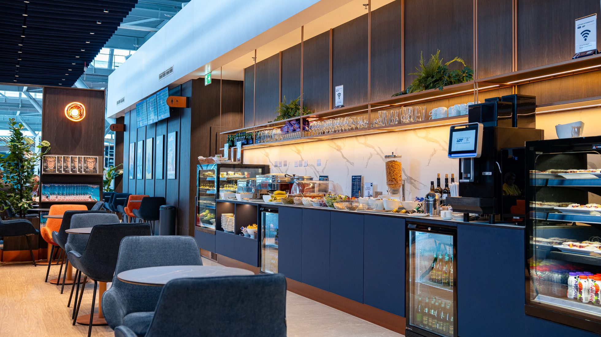 Luksusowa strefa wypoczynku w lotniskowym salonie biznesowym - przy strefie restauracyjnej stoliki kawowe z granatowymi fotelami.