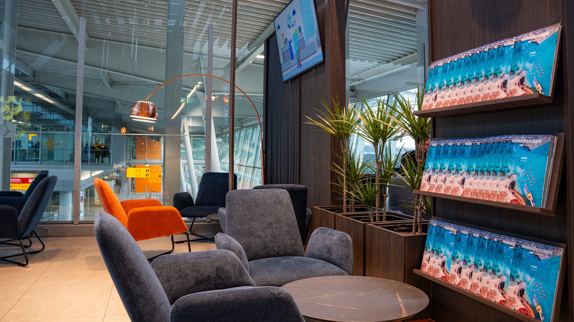 Graue Sessel an einem Couchtisch in der Polonez Business Lounge in Warschau, neben einem Regal mit Kaleidoscope-Magazinen