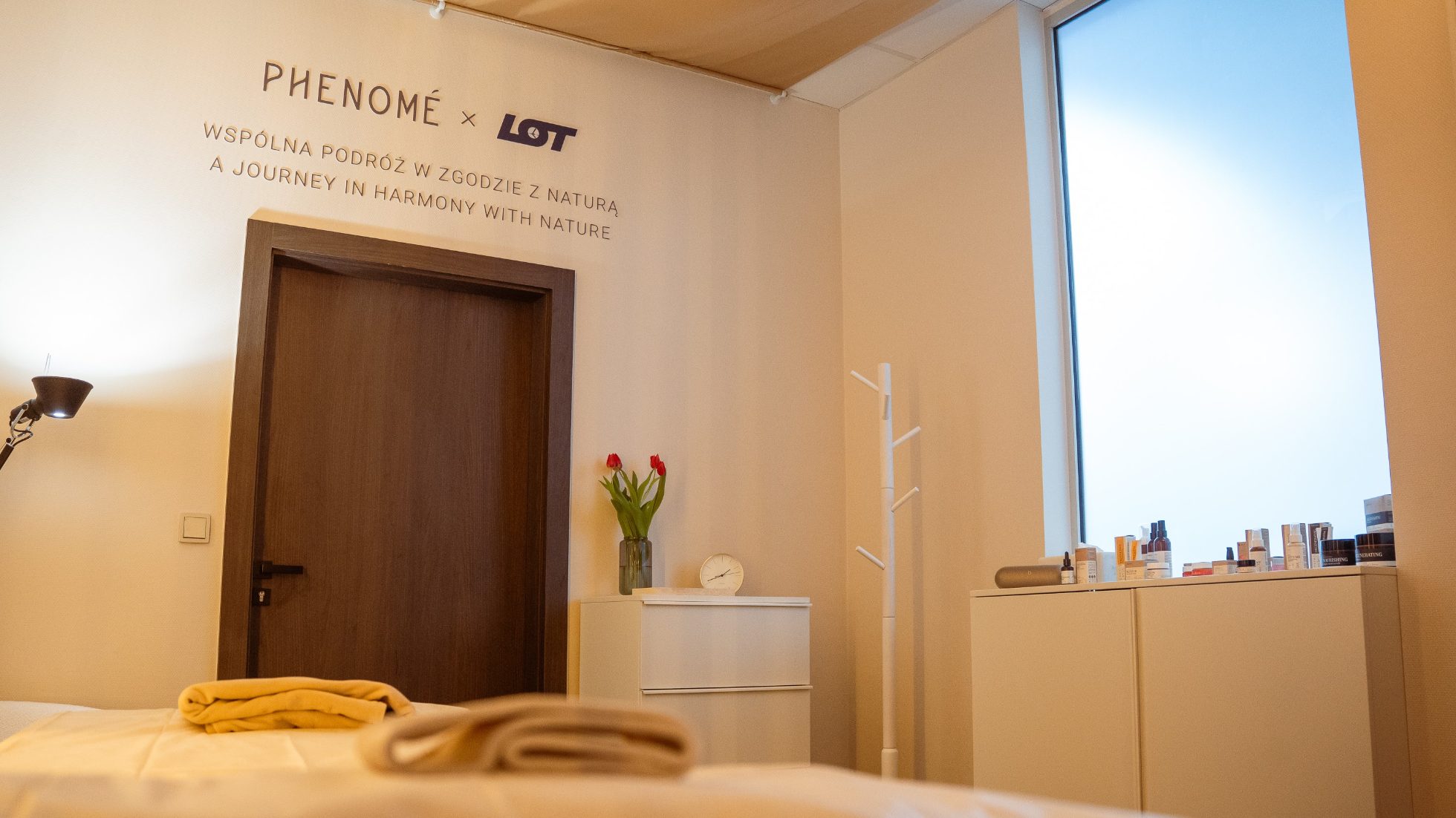 Strefa SPA Phenome w LOT Business Lounge Polonez - drzwi, biała szafka z kwiatkami oraz napis LOT i Phenome