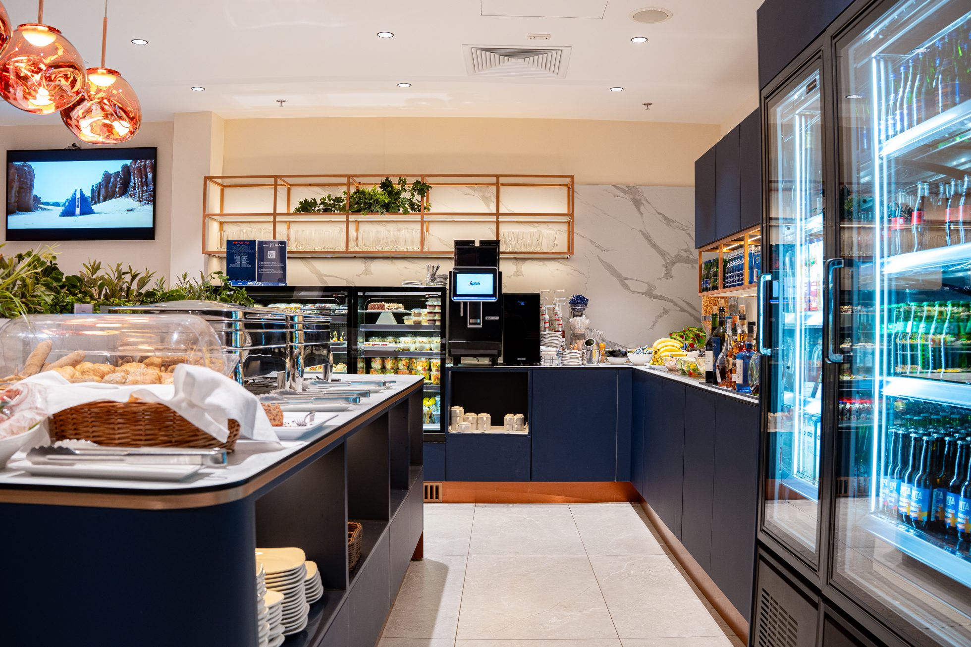 Polonez Gold Lounge - an open space with orange chairs and sofas, navy blue walls with the Crane logo. Catering area with hot meals, snacks and drinks. Relaxation area with armchairs and dimmed lighting.