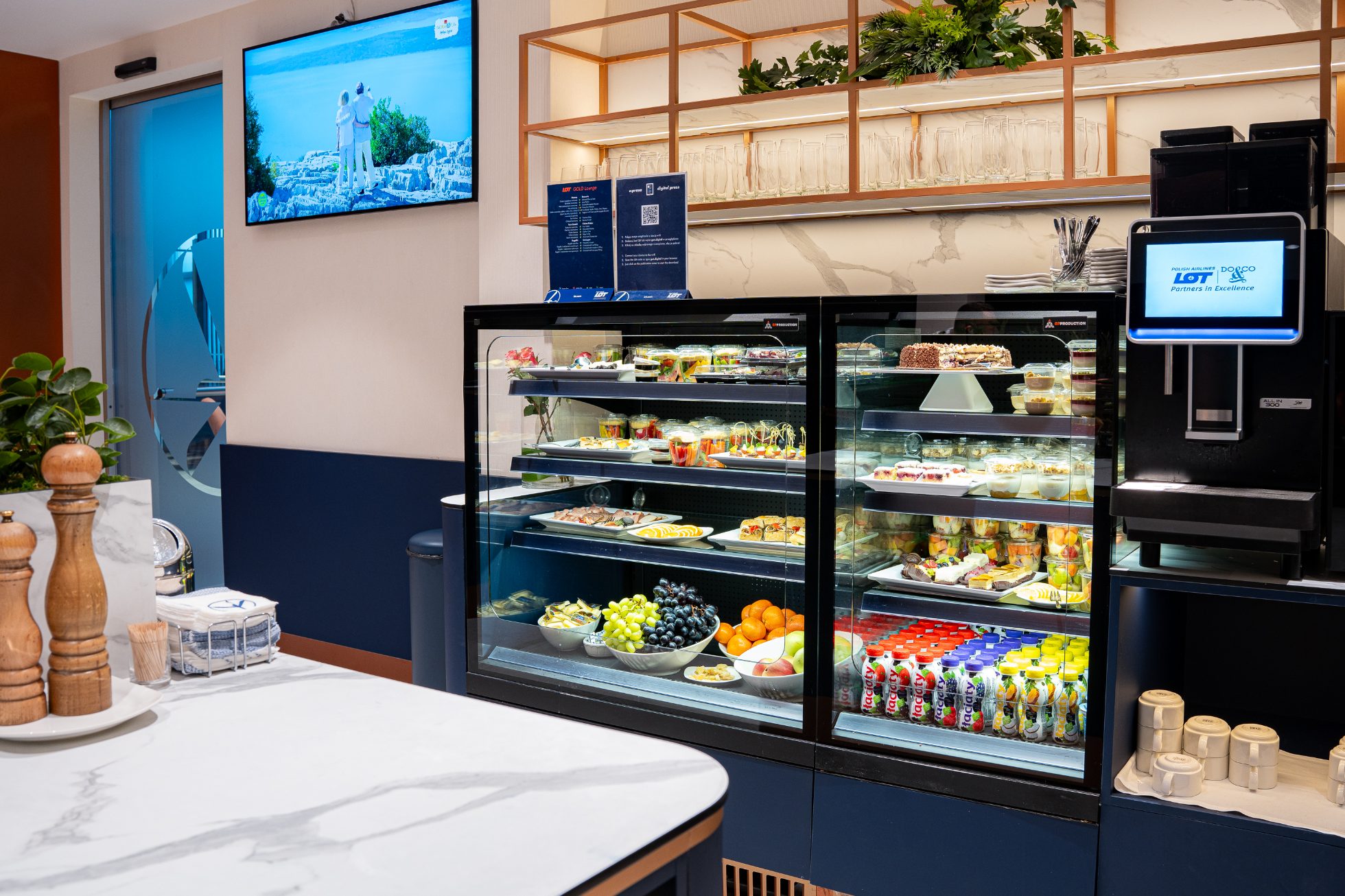 Polonez Gold Lounge - an open space with orange chairs and sofas, navy blue walls with the Crane logo. Catering area with hot meals, snacks and drinks. Relaxation area with armchairs and dimmed lighting.