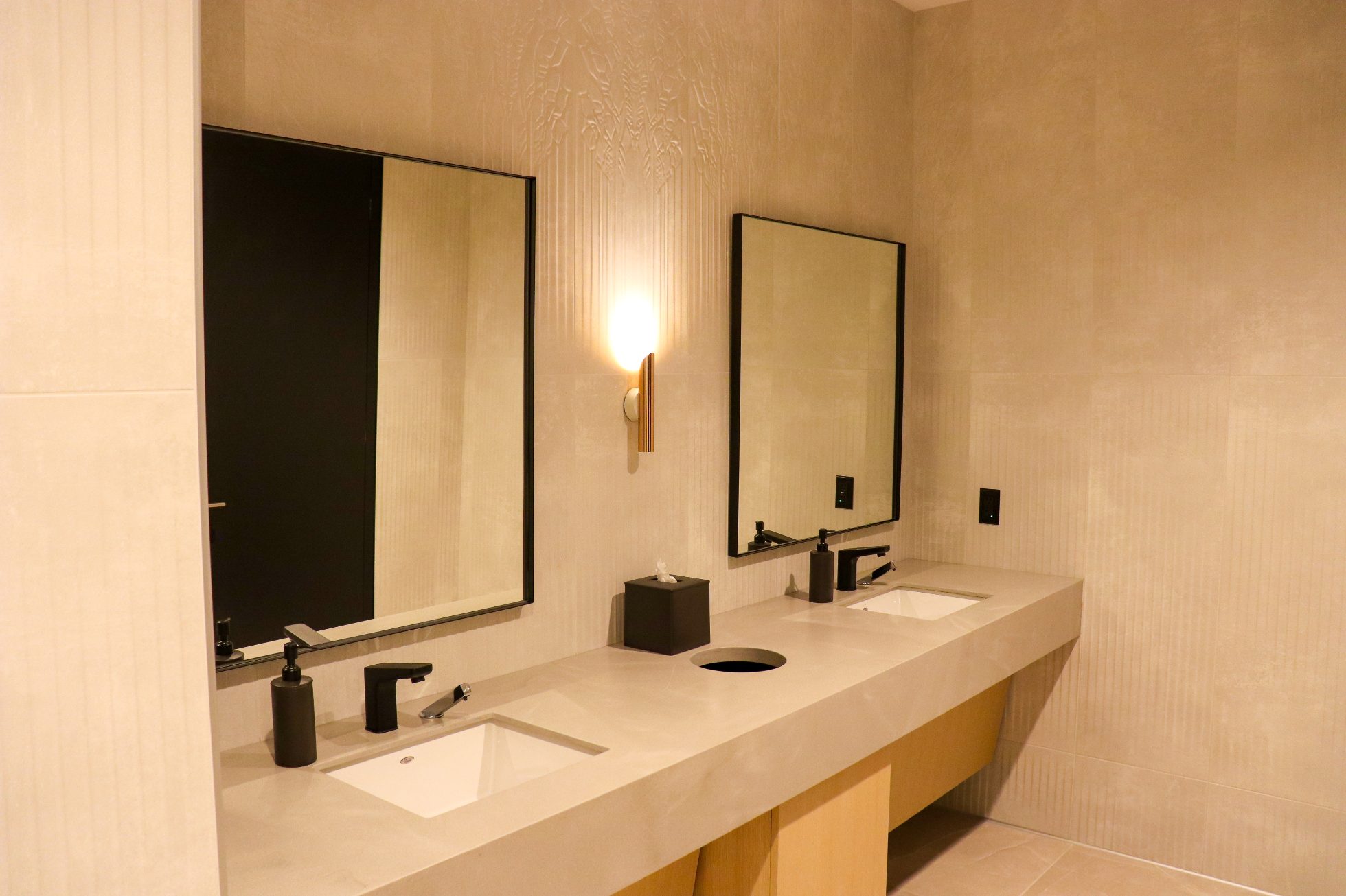 LOT Business Lounge in Chicago - reception area with illuminated LOT logo. Public space with yellow sofas, copper lamps and tables with white marble tops. Blue carpets. High ceiling and huge panoramic windows overlooking the airport. Large bar with backlights