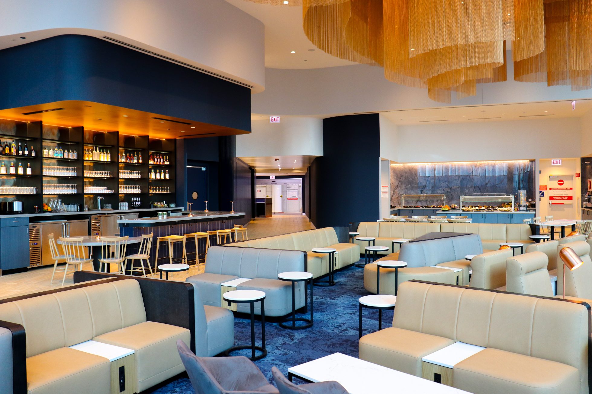 View of a business lounge space in Chicago, modern interior, stylish light sofas and round tables nearby, a bar visible on a granite wall in the back.