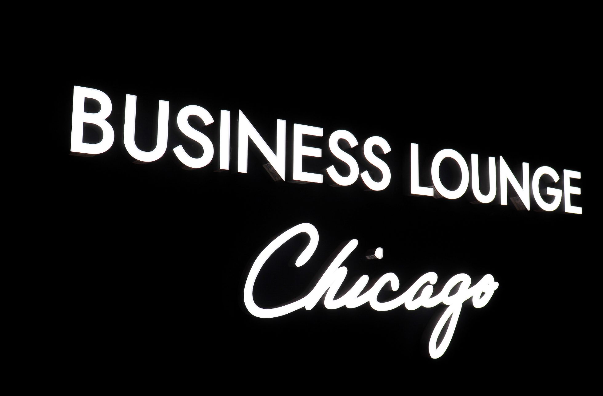 LOT Business Lounge in Chicago - reception area with illuminated LOT logo. Public space with yellow sofas, copper lamps and tables with white marble tops. Blue carpets. High ceiling and huge panoramic windows overlooking the airport. Large bar with backlights