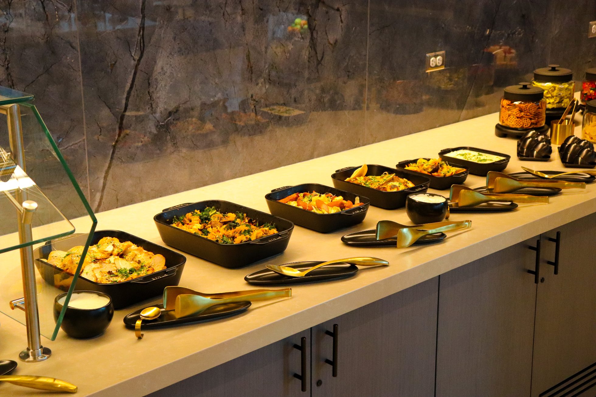 LOT Business Lounge in Chicago - reception area with illuminated LOT logo. Public space with yellow sofas, copper lamps and tables with white marble tops. Blue carpets. High ceiling and huge panoramic windows overlooking the airport. Large bar with backlights