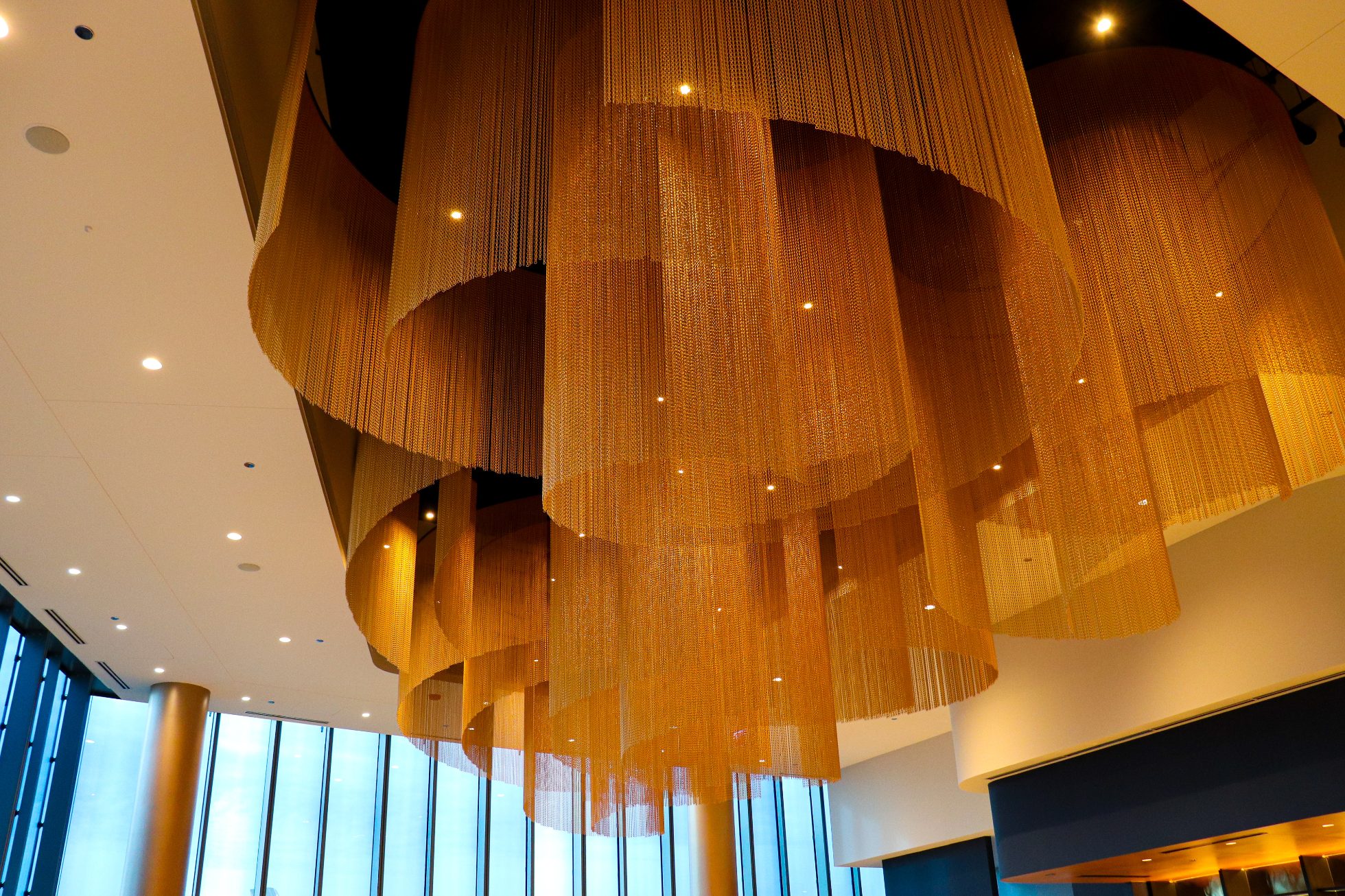 LOT Business Lounge in Chicago - reception area with illuminated LOT logo. Public space with yellow sofas, copper lamps and tables with white marble tops. Blue carpets. High ceiling and huge panoramic windows overlooking the airport. Large bar with backlights