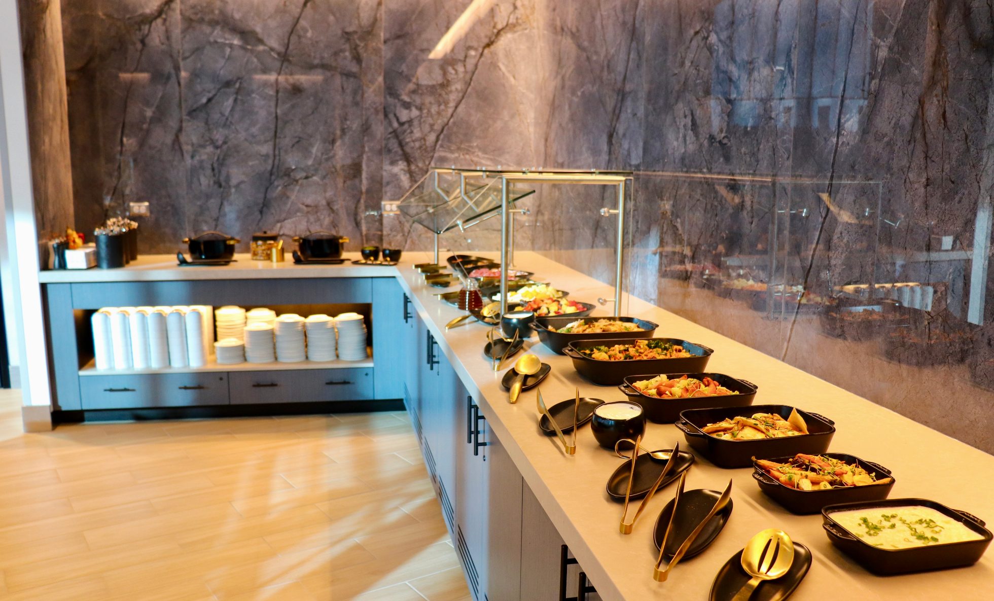 LOT Business Lounge in Chicago - reception area with illuminated LOT logo. Public space with yellow sofas, copper lamps and tables with white marble tops. Blue carpets. High ceiling and huge panoramic windows overlooking the airport. Large bar with backlights