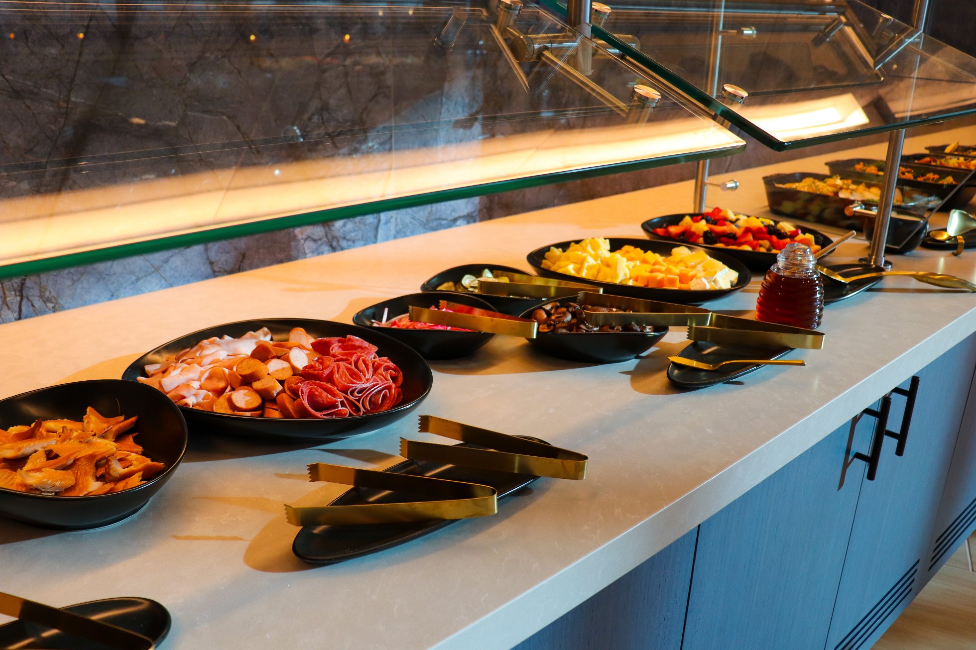 LOT Business Lounge in Chicago - reception area with illuminated LOT logo. Public space with yellow sofas, copper lamps and tables with white marble tops. Blue carpets. High ceiling and huge panoramic windows overlooking the airport. Large bar with backlights