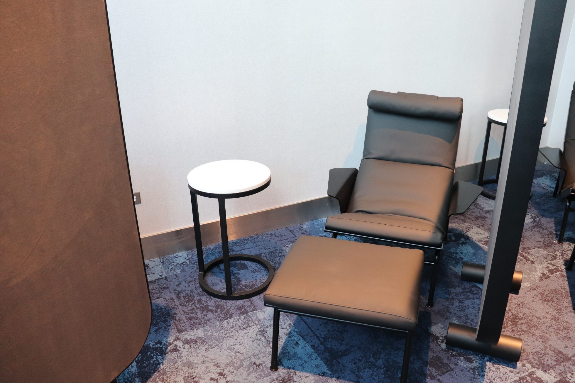 LOT Business Lounge in Chicago - reception area with illuminated LOT logo. Public space with yellow sofas, copper lamps and tables with white marble tops. Blue carpets. High ceiling and huge panoramic windows overlooking the airport. Large bar with backlights
