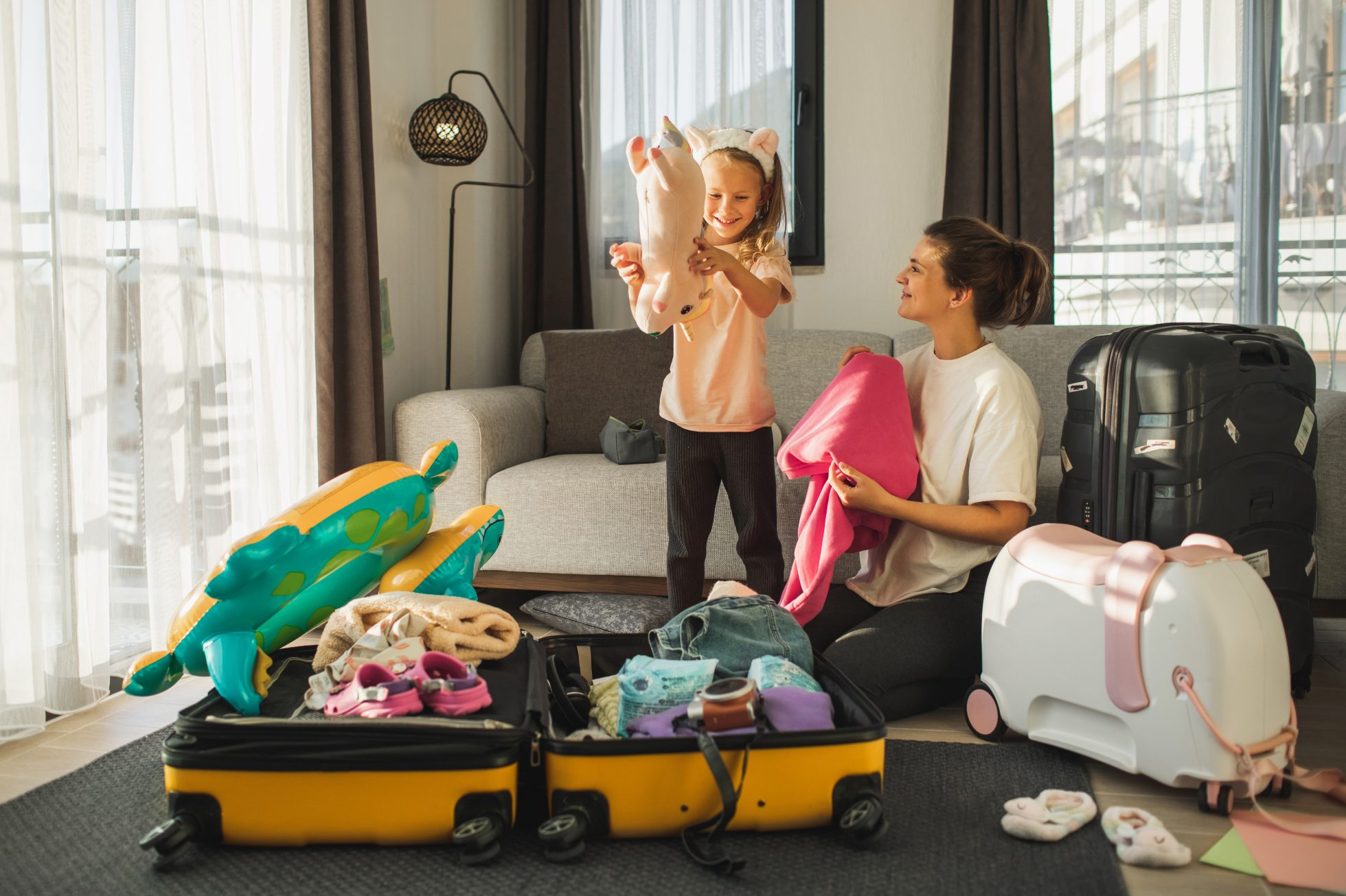 A family with a mother and a little blonde girl prepares to go on vacation, luggage on the floor, folding clothes in a large yellow suitcase. what to take on vacation with a child?