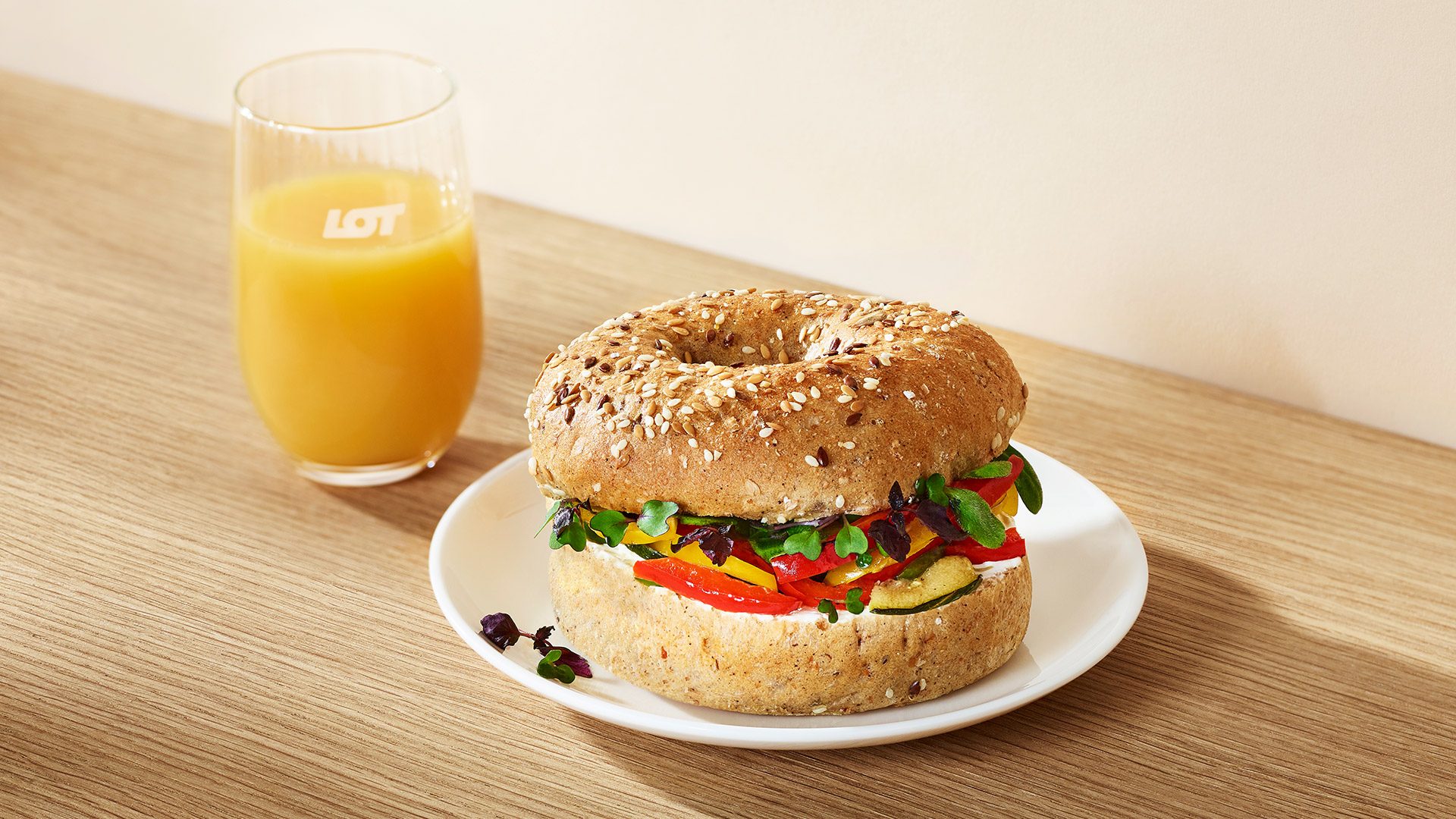 Wieloziarnisty bajgiel z kremowym serkiem śmietankowym i kolorowymi warzywami z grilla: papryką i cukinią, dopełniony świeżą rzeżuchą Shiso.