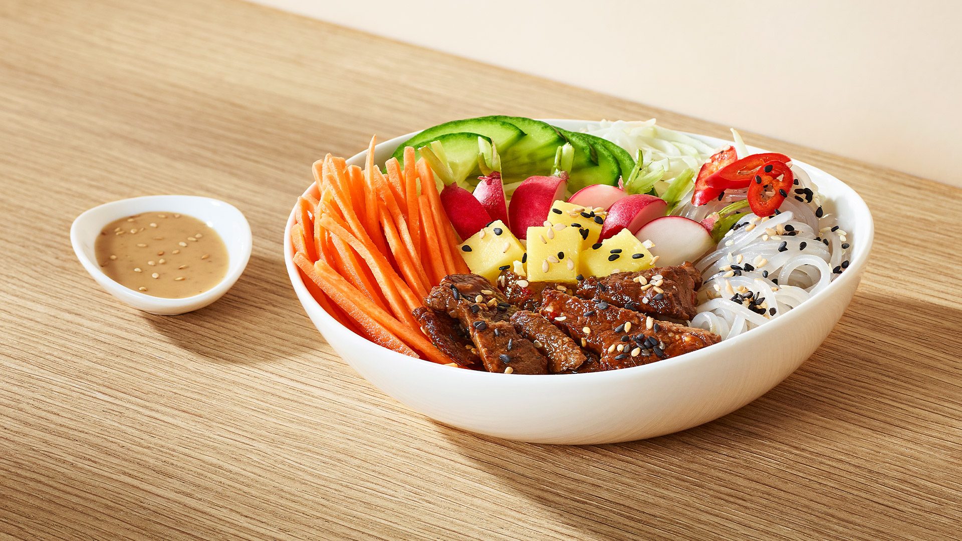 Beef salad – Poke Bowl  An oriental salad with vermicelli noodles, beef in Korean sauce, crispy cabbage, fresh carrots, cucumber, radish, and mango, sprinkled with roasted black sesame seeds. 