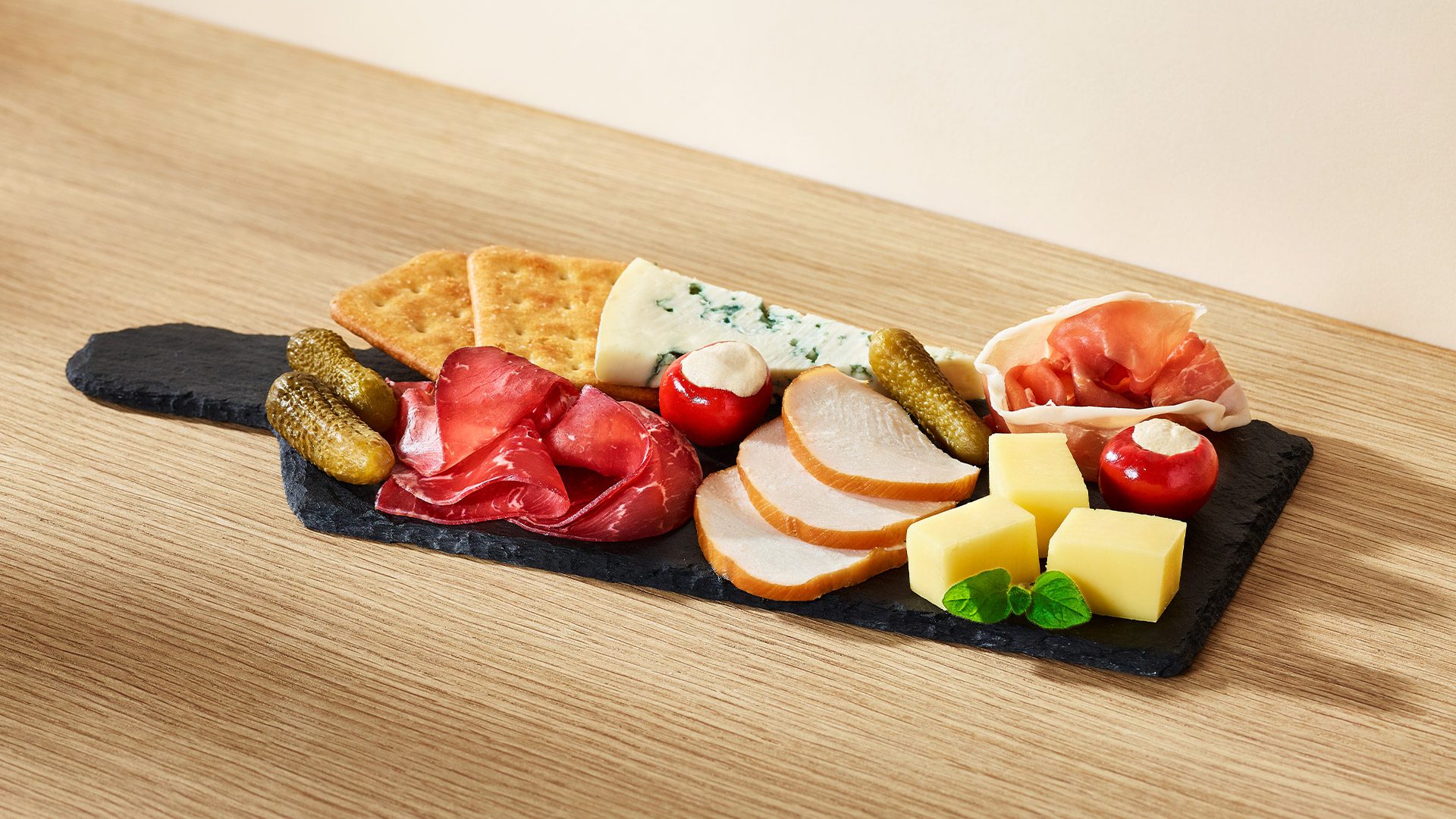 Wykwintna taca z dojrzewającą szynką, wędzonym kurczakiem, delikatną breasolą oraz aromatycznymi serami Lazur i Cheddar z dodatkiem chrupiących krakersów, korniszona i papryczek z serem.