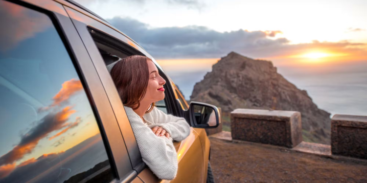 A smiling woman is sitting in a car and admiring the sunset.