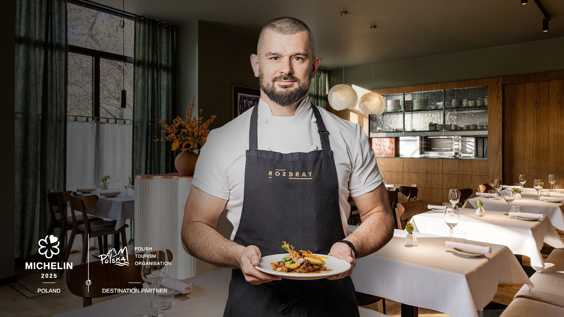 Chef Bartosz Szymczak of Rozbrat 20 holding a dish. The interior of the restaurant in the background.