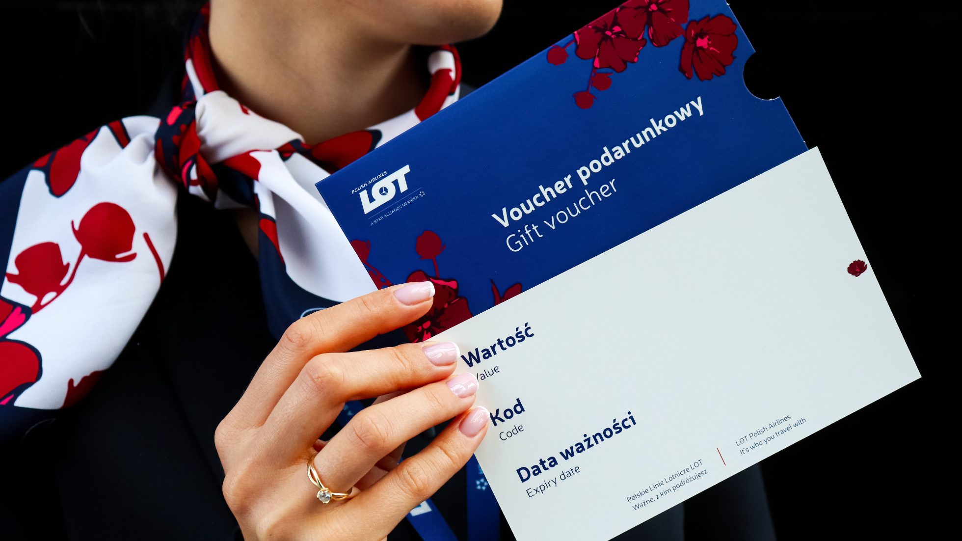 Voucher podarunkowy trzymany przez osobę w mundurze LOT