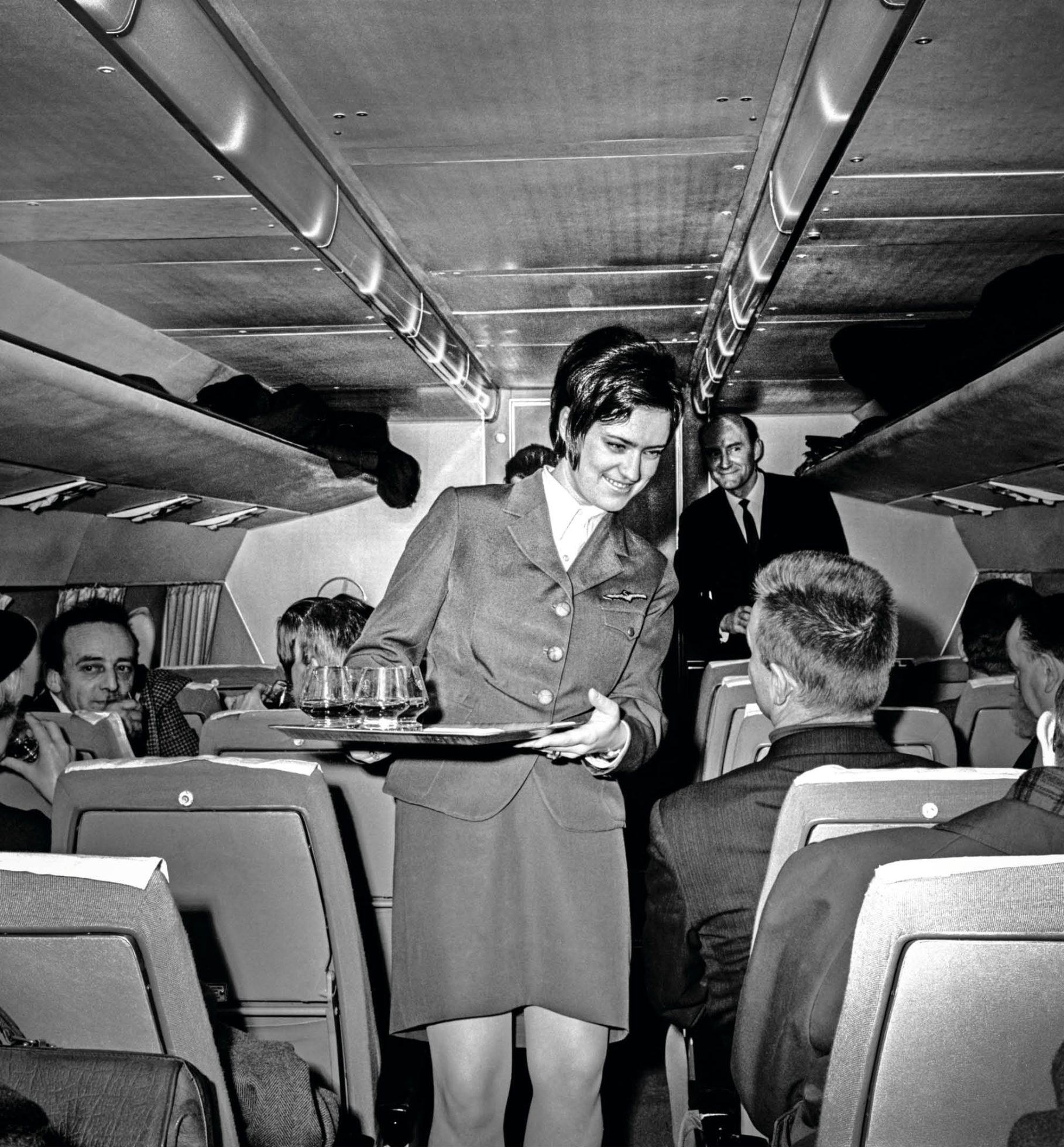 Fekete-fehér fotó egy stewardessről, amint dolgozik a repülőgépen.
