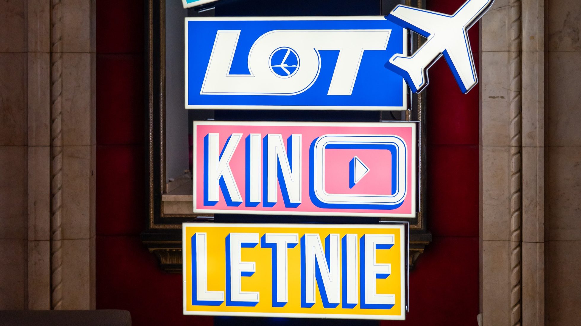Neon w kolorze niebieskim, różowym i żółtym z napisem LOT Kino Letnie i samolotem