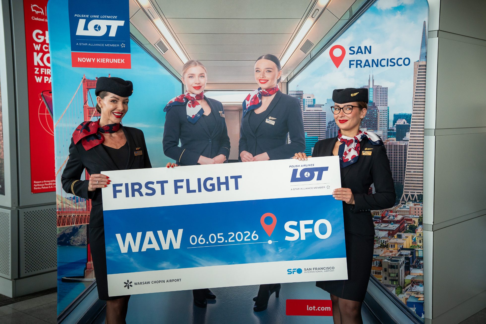Two LOT flight attendants in uniform holding a sign to mark the launch of the San Francisco route