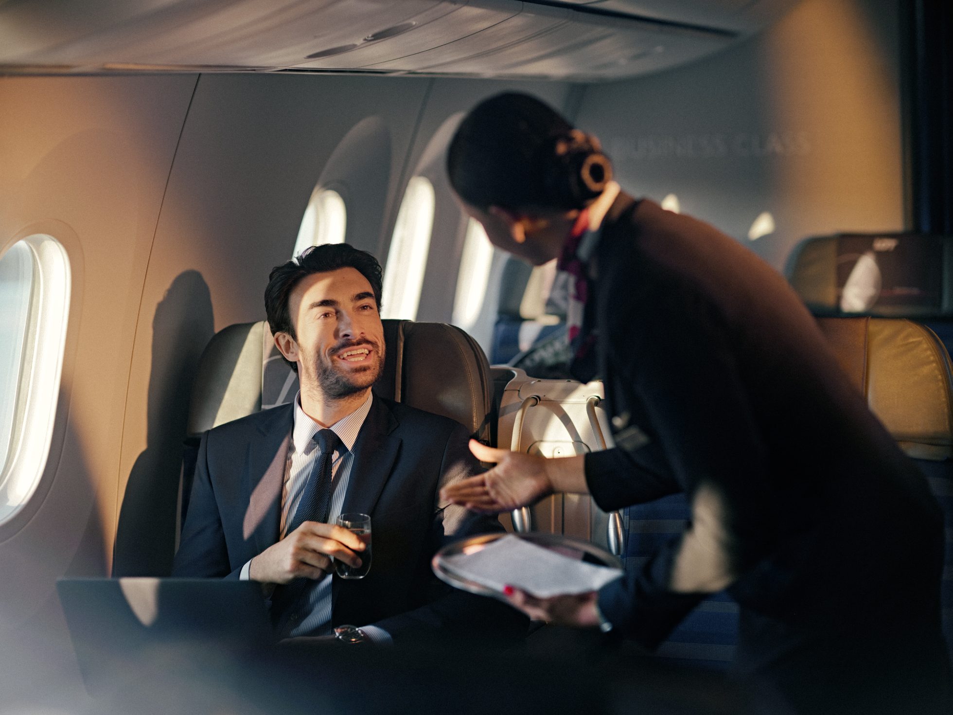 Stewardesa podająca pasażerowi biznesowemu szklankę wody na pokładzie Dreamlinera