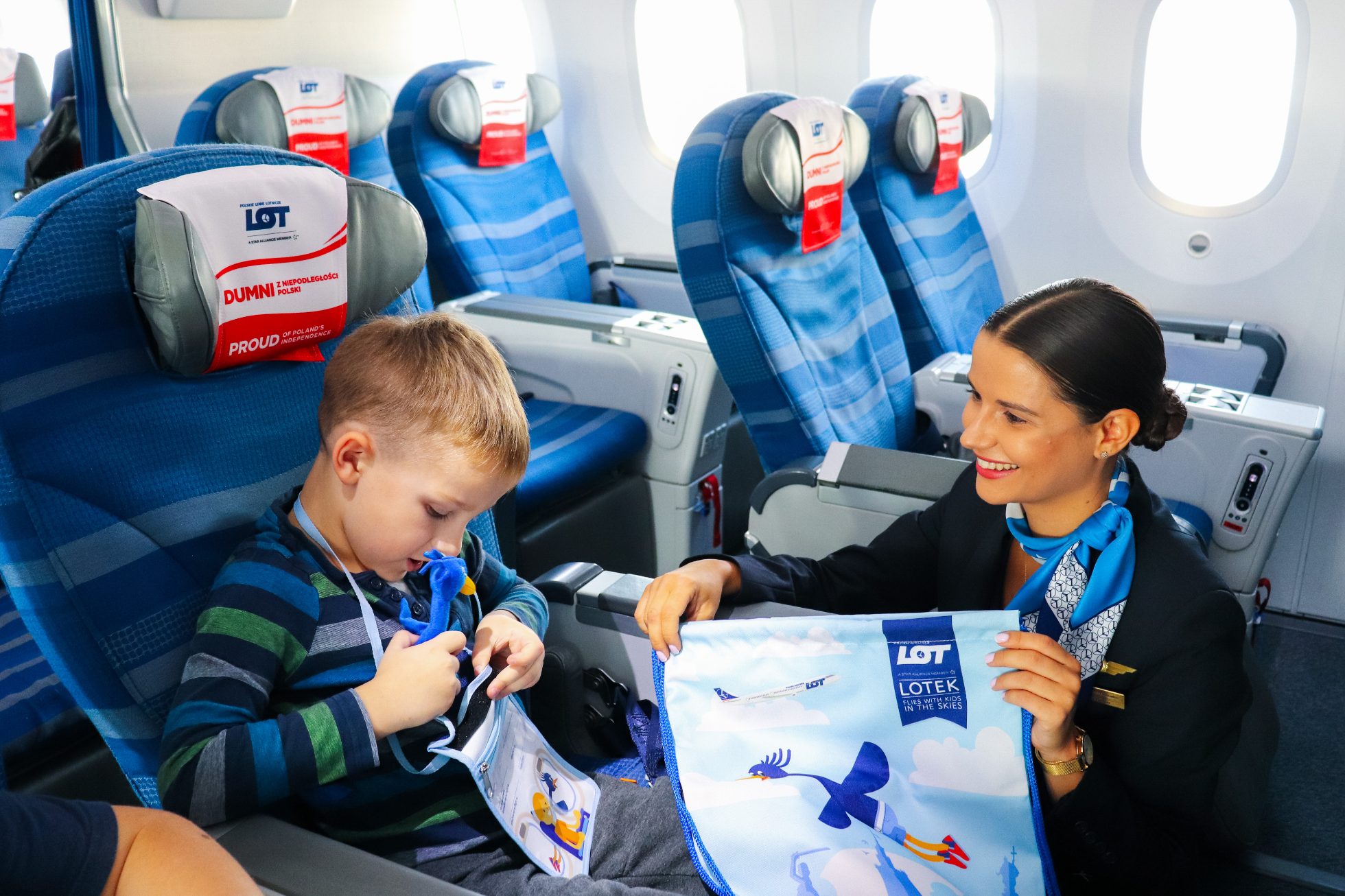 Un enfant est assis dans un siège d'avion, tient un livre coloré et sourit.