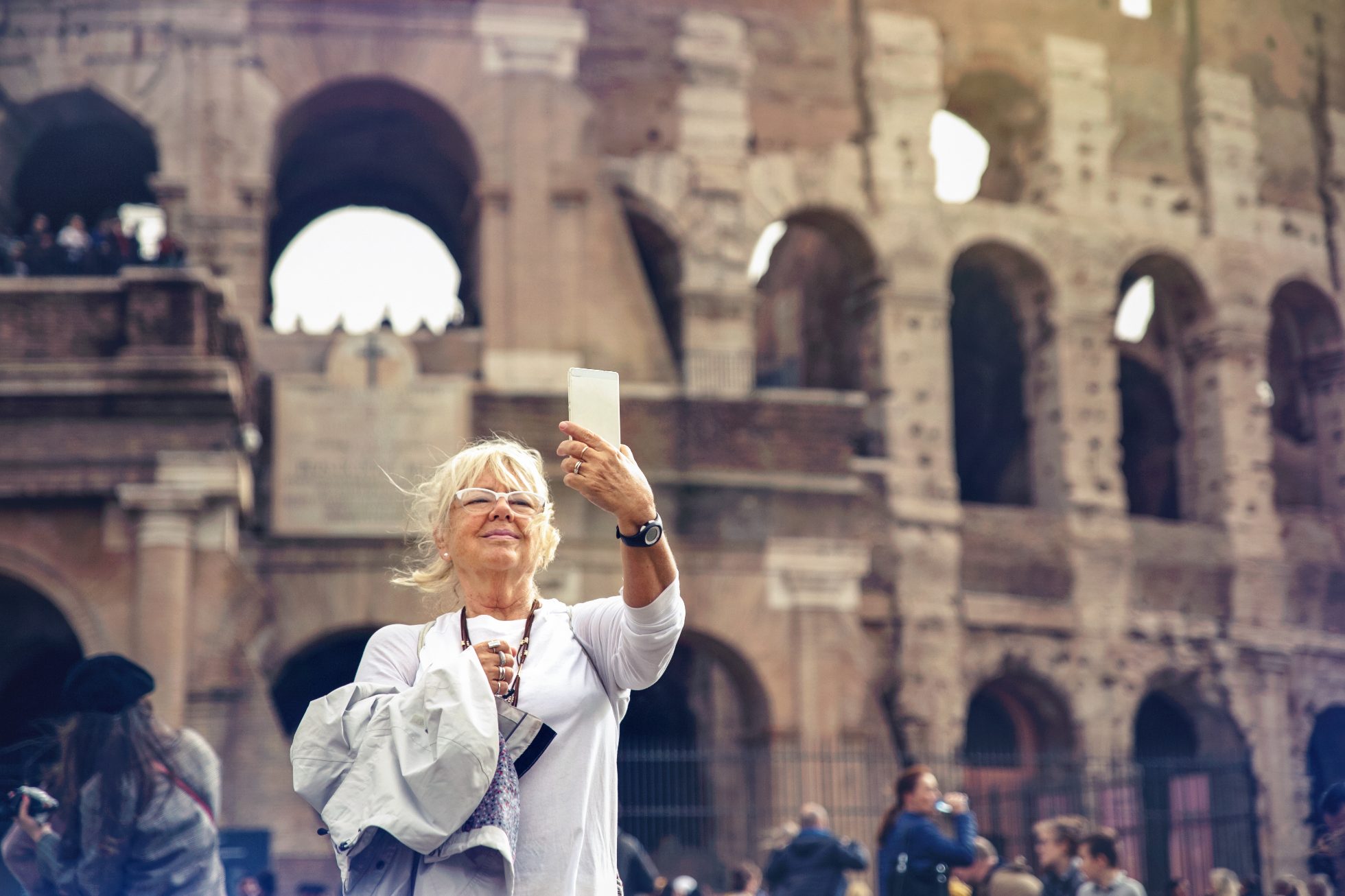 Starsza kobieta o blond włosach robi selfie przed rzymskim Koloseum