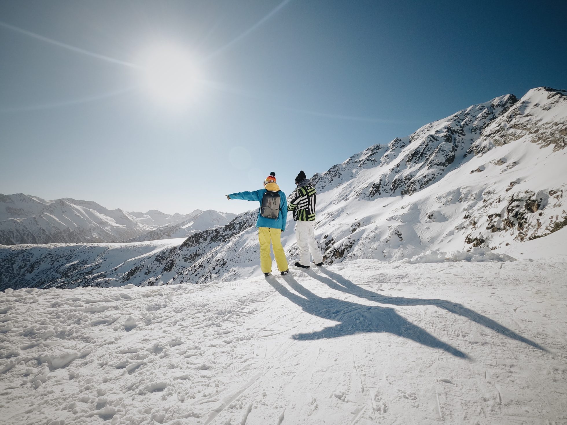A couple of people are enjoying the views from a ski slope on a sunny day - where to ski in Europe?