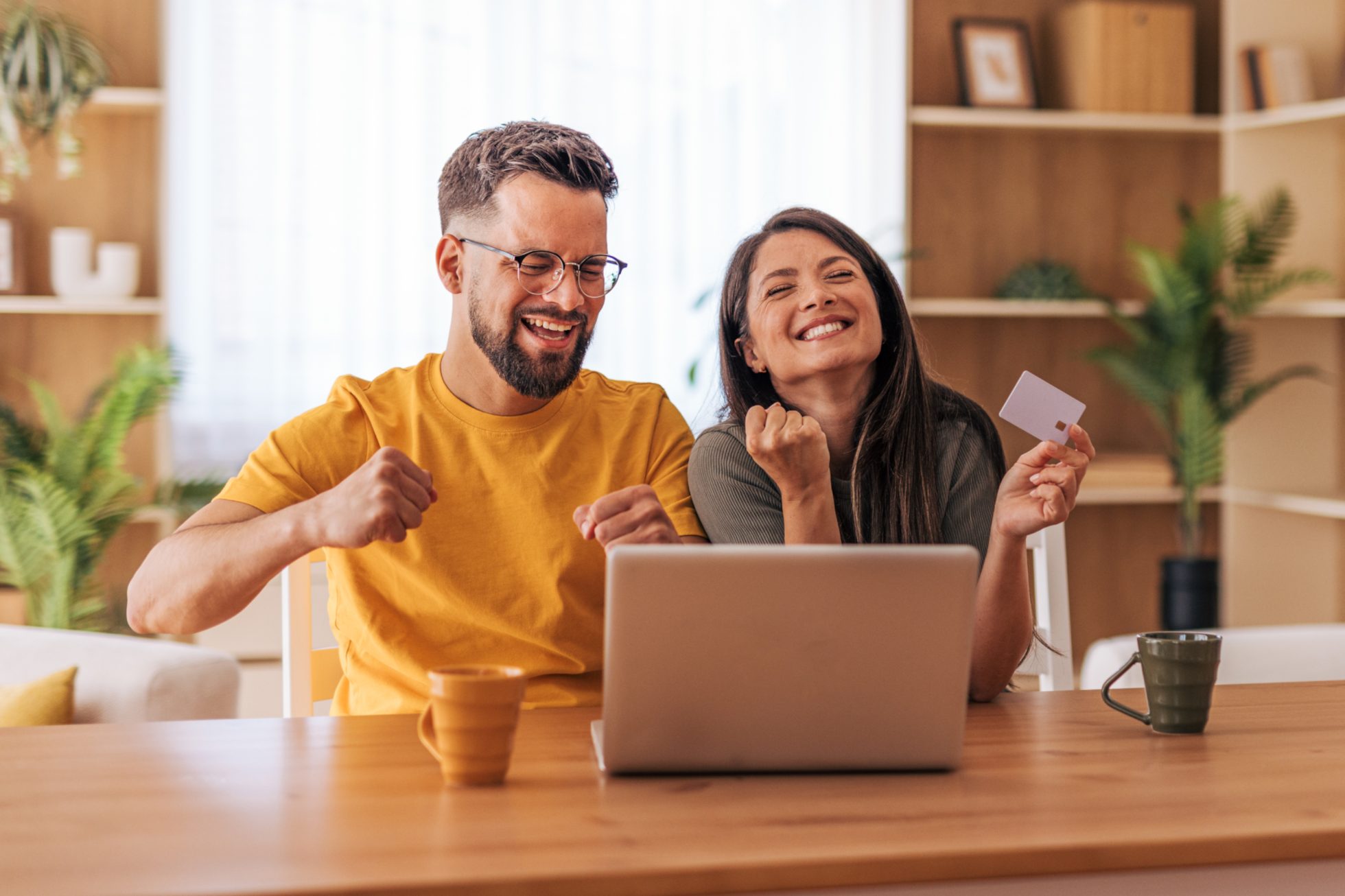 A man and a woman are sitting at a table with an open laptop and are enjoying making a payment via the internet.