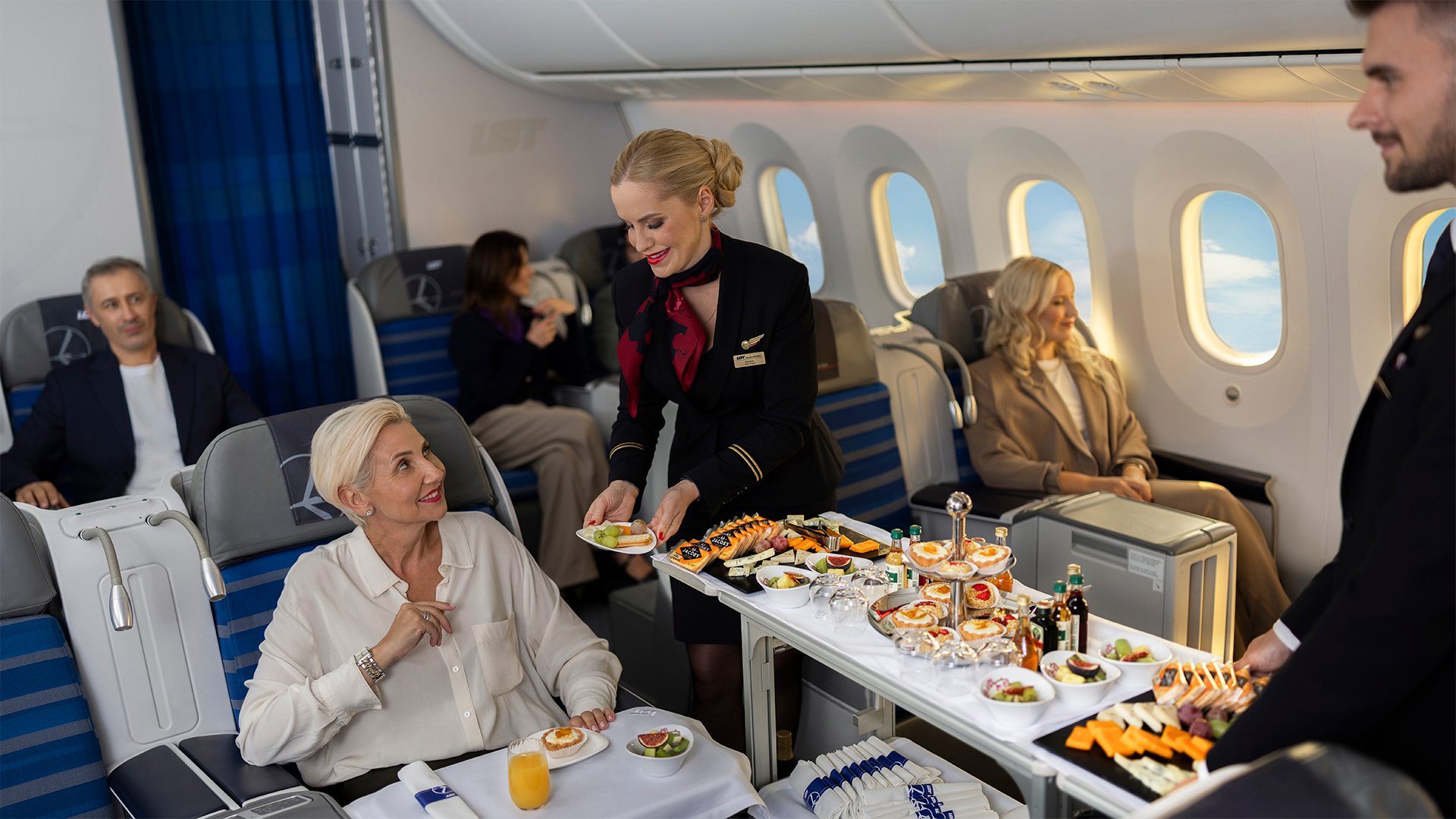 La tripulación de cabina de LOT Polish Airlines atiende a los pasajeros de LOT Business Class. Sirviendo postres y selecciones de quesos desde un carrito.