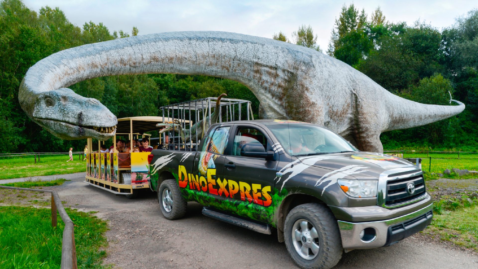 A carriage with children passing by a dinosaur statue in the Dinopark in Ostrava.