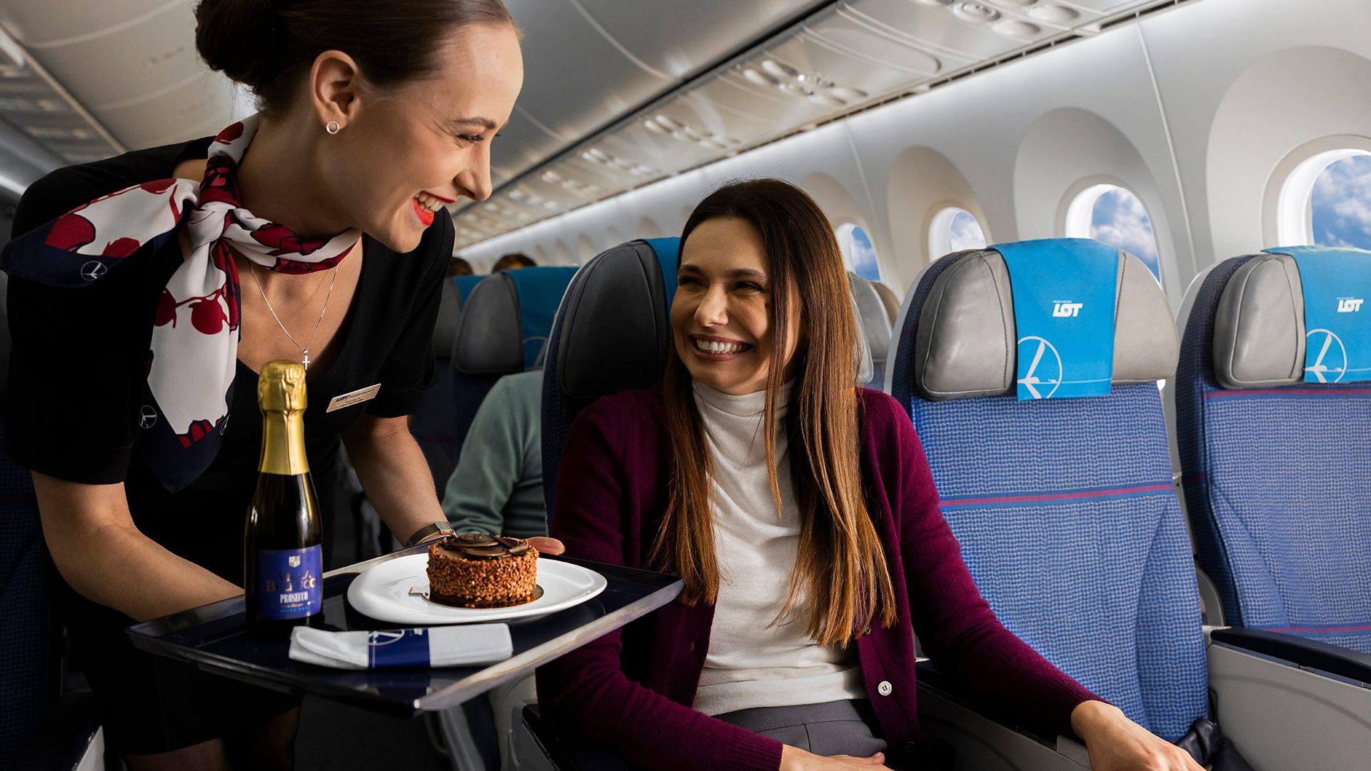Une hôtesse de l'air servant un passager surpris avec un gâteau au chocolat et du prosecco à bord d'un Boeing 787 Dreamliner