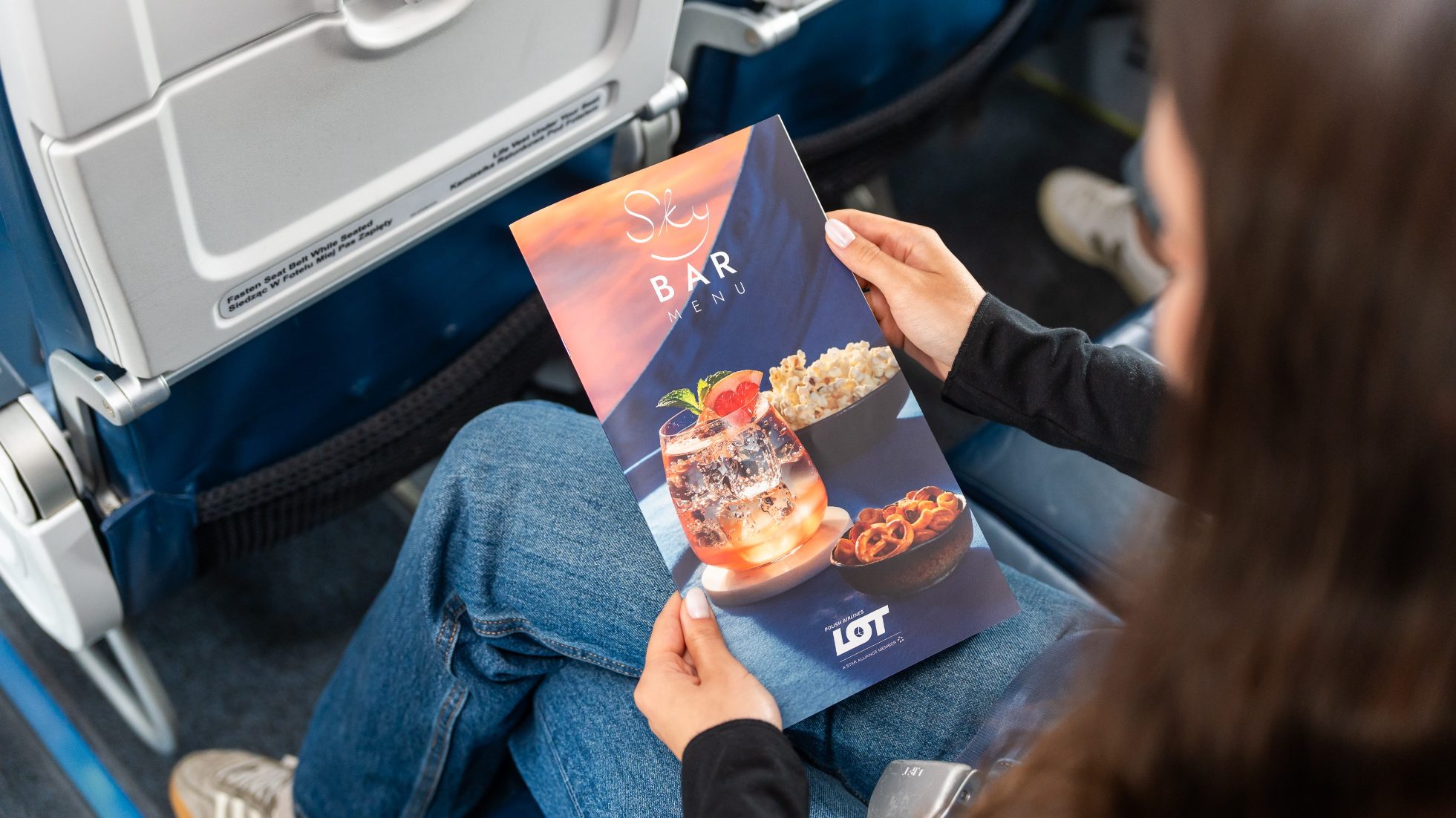 Passenger sitting in seat holding Sky Bar catalog in hand